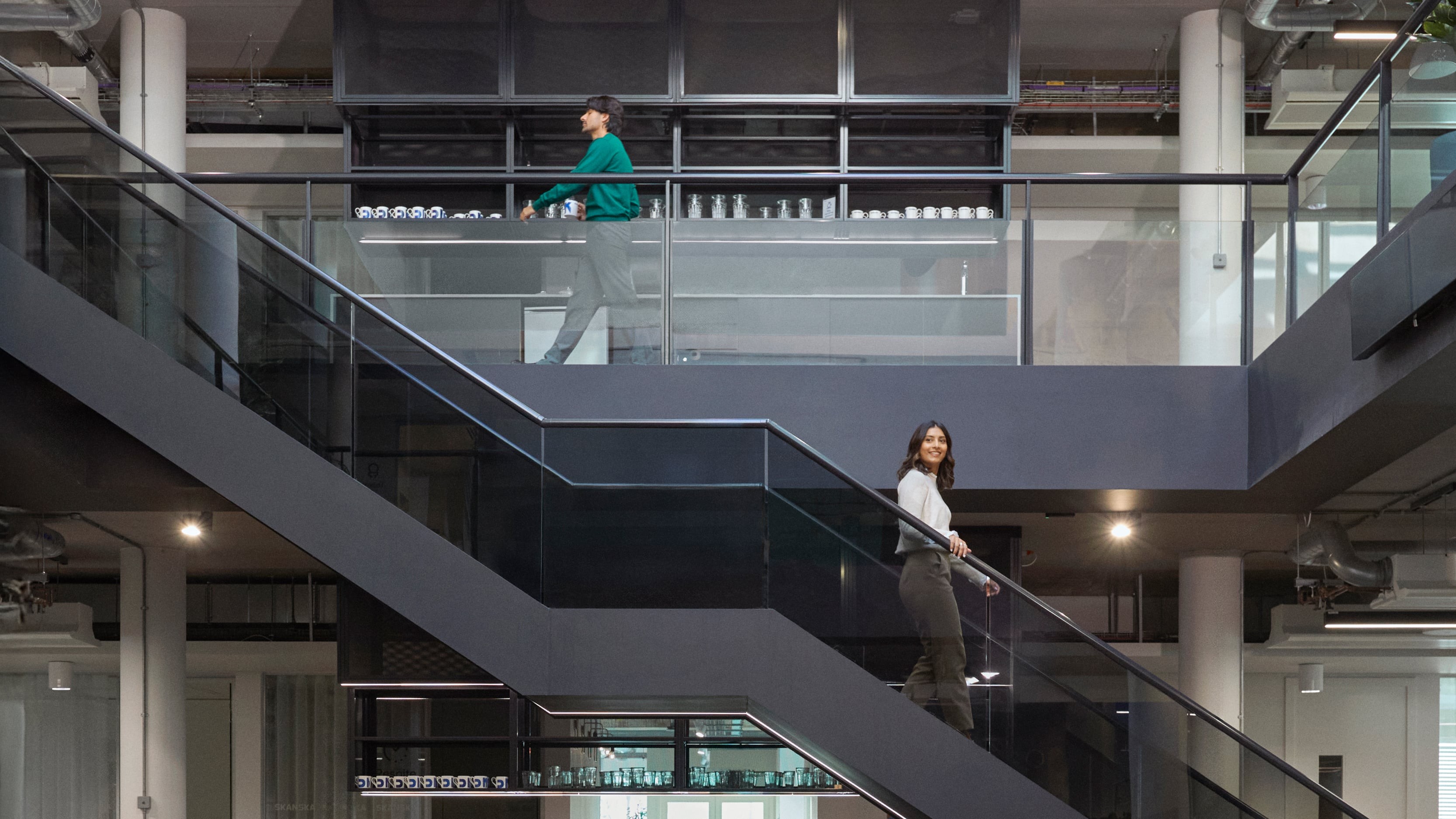 Two people walking on separate staircases in a modern office building interior.