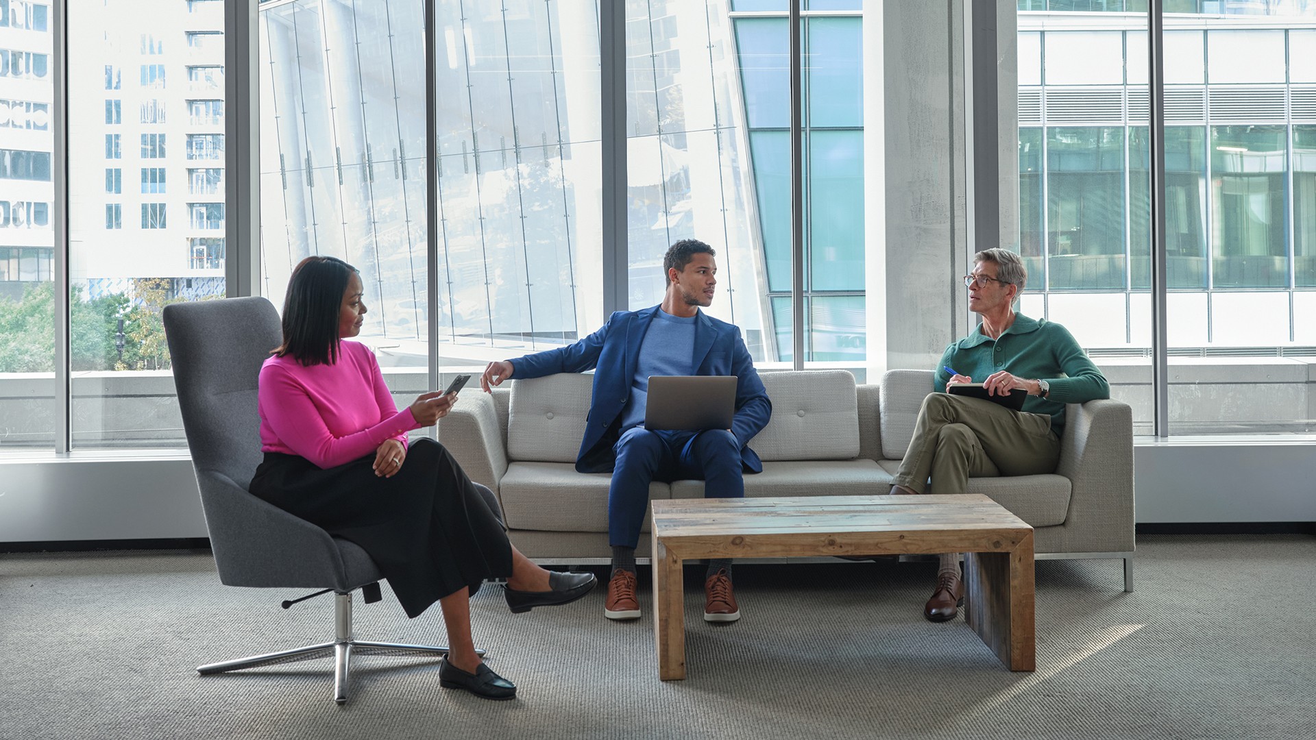 Modern Office Meeting with Diverse Professionals Three people engaged in a business meeting in a modern office with large windows.