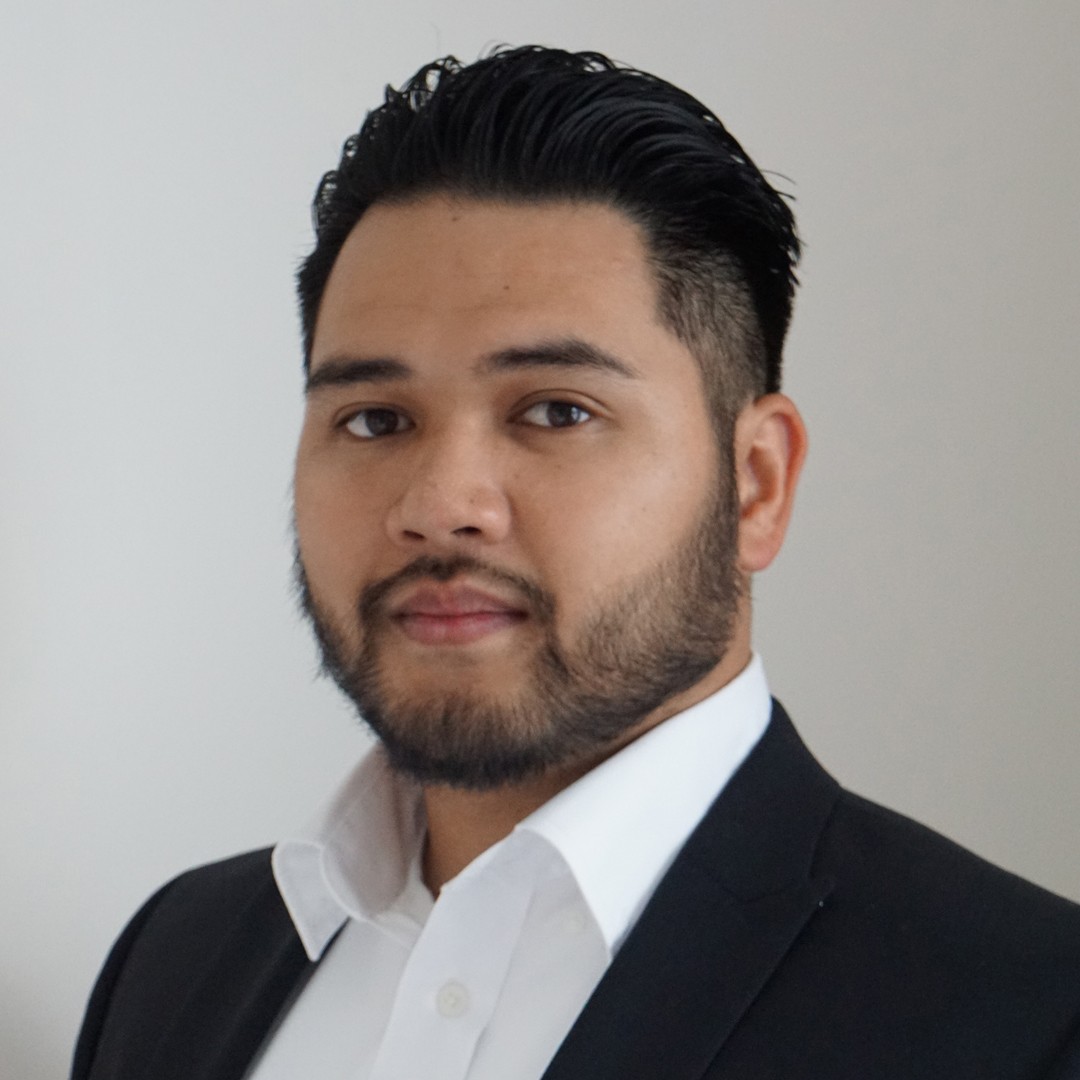 Professional Portrait in Suit Jacket Person wearing a dark suit jacket and white collared shirt, standing against a plain light background.