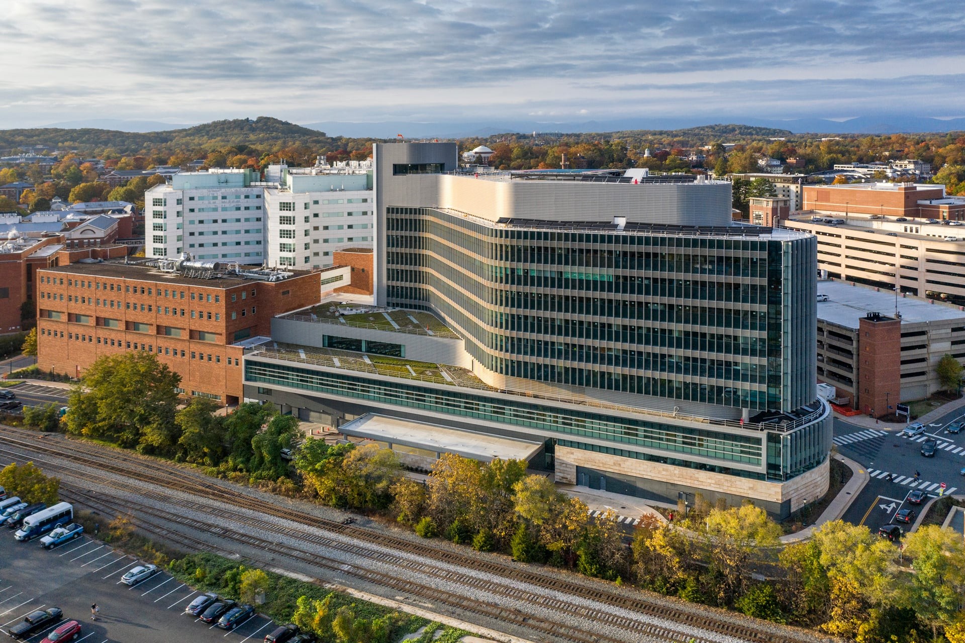 Modern multi-story hospital building with glass windows and surrounding autumn trees.
