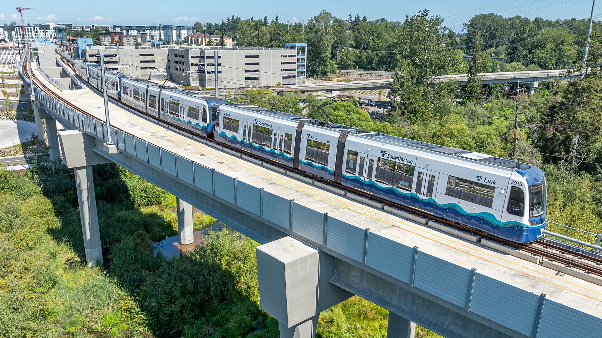 Seattle Light Rail Train on Elevated Track in Scenic View Elevated light rail train traveling through a green suburban area, with modern apartments in view.