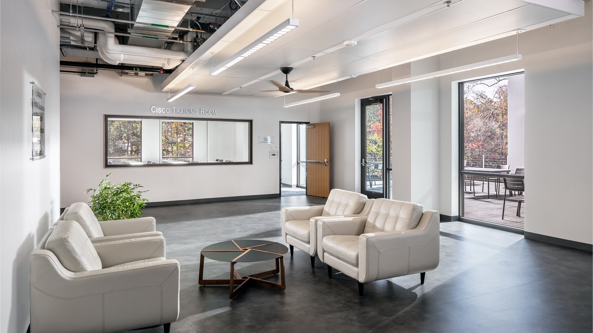 Modern Office Lounge with Stylish White Seating Modern lounge area with white seating, a round table, and large windows in a training facility.