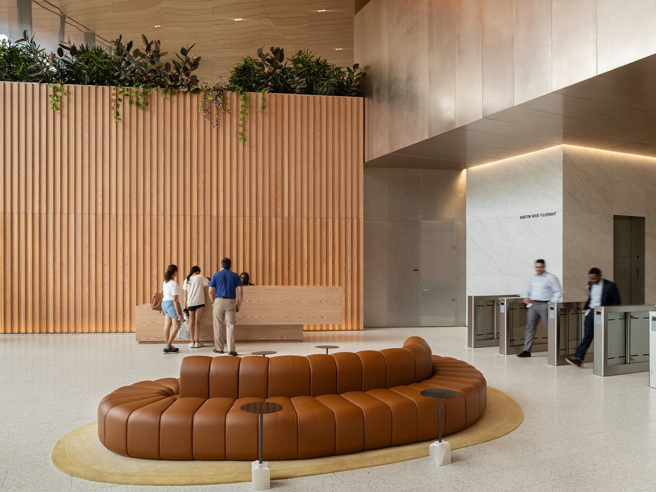 Office Lobby with Stylish Seating and Wooden Accents Office lobby with a circular brown couch, wood paneling, plants, and people at the reception desk.