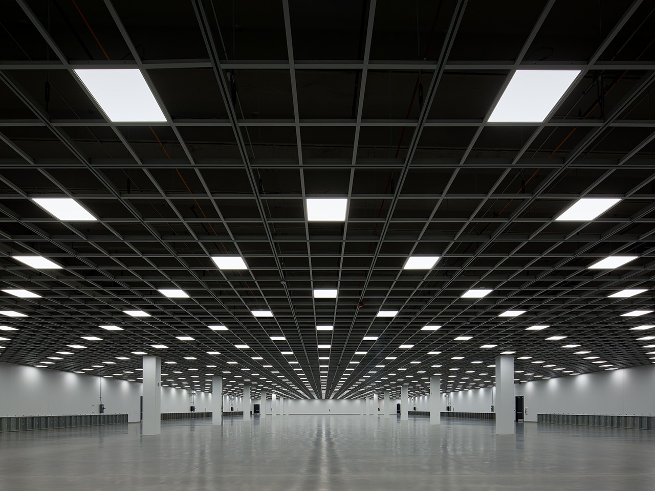 Spacious Empty Data Center with Grid Ceiling Design Vast empty room with grid ceiling, bright lights, and white columns creating a symmetrical pattern.