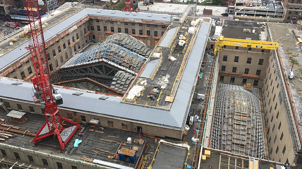 Aerial view of a construction site with cranes and curved glass roof structures.