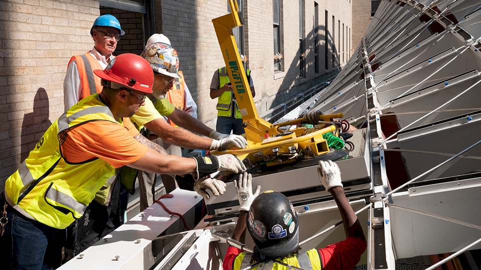 Construction workers installing glass panels on a modern building facade using safety gear.