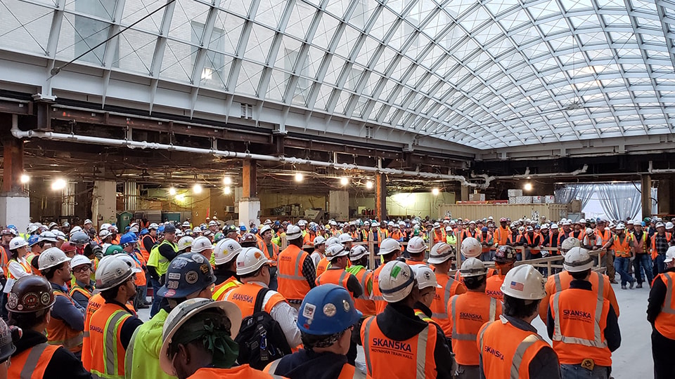 Large group of construction workers wearing helmets and vests inside a building site.