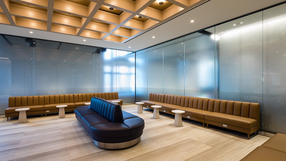 Modern office lounge with brown leather sofas, glass walls, and wooden ceiling design.