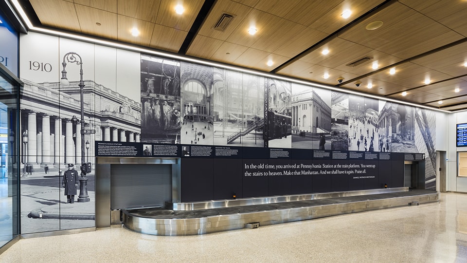 Historic black-and-white mural of Pennsylvania Station from 1910 inside a modern terminal.