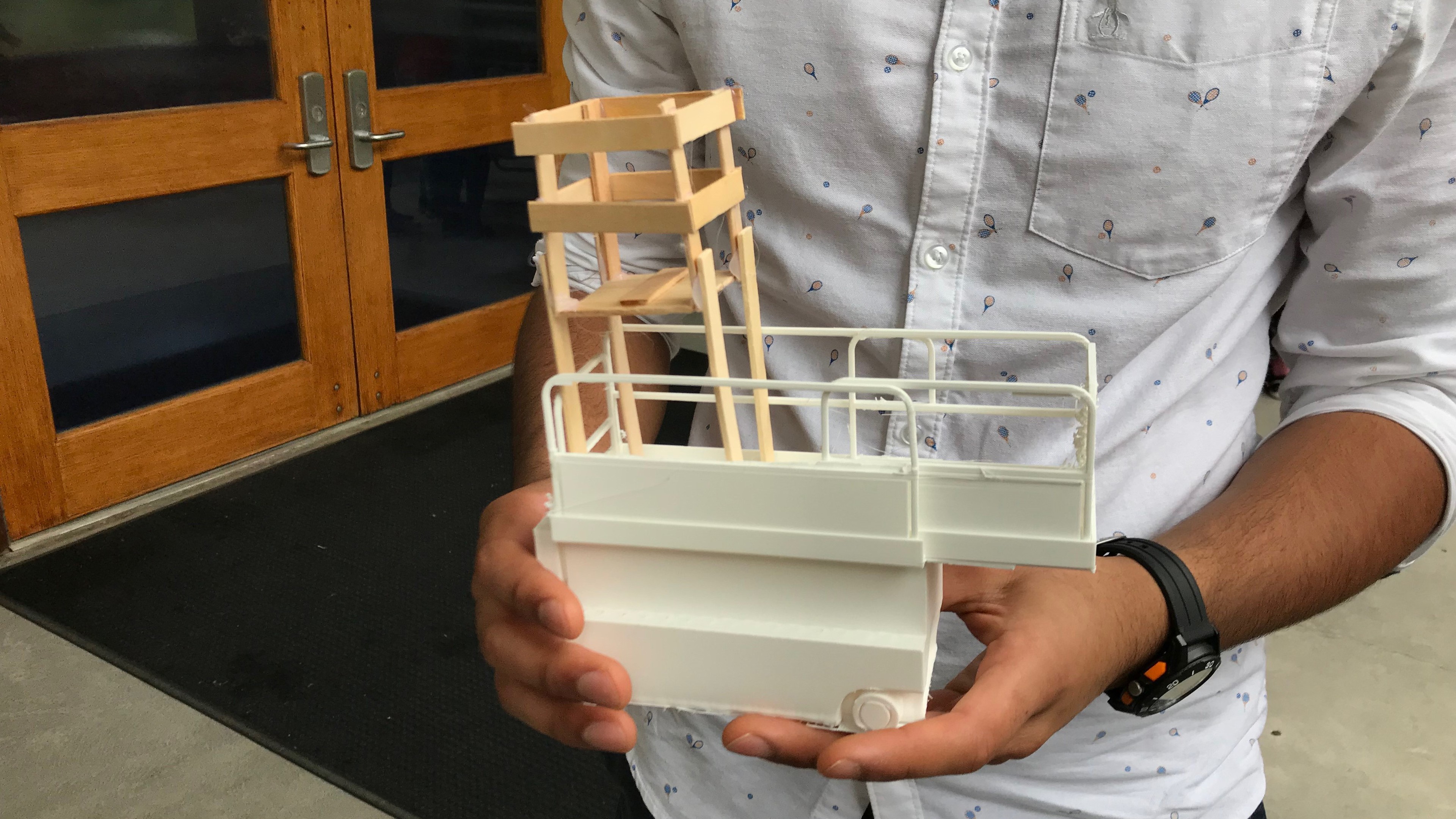 Person holding a detailed architectural model of a building structure with railing.