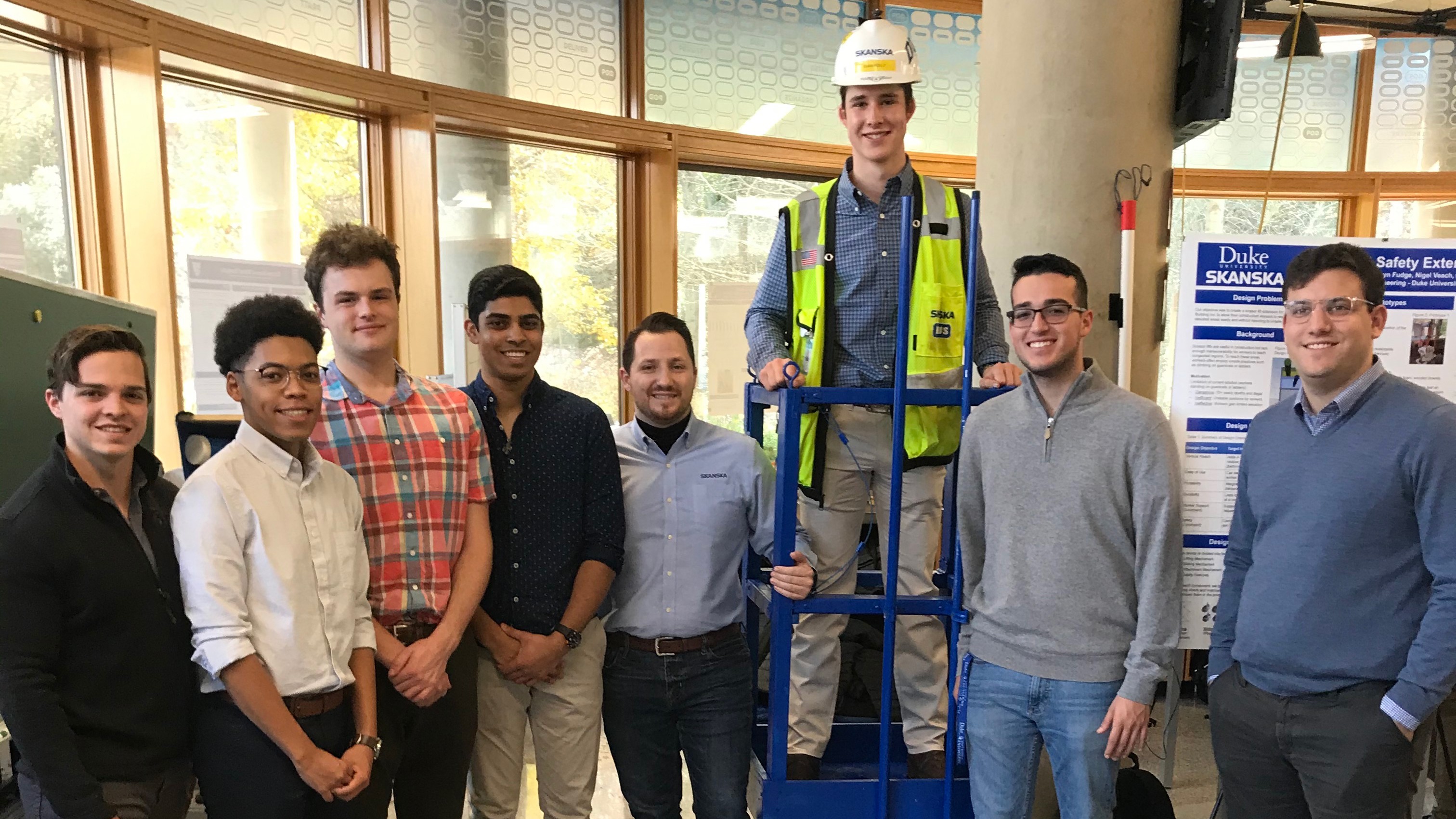 Group of construction workers in safety gear posing indoors with equipment and safety signs.