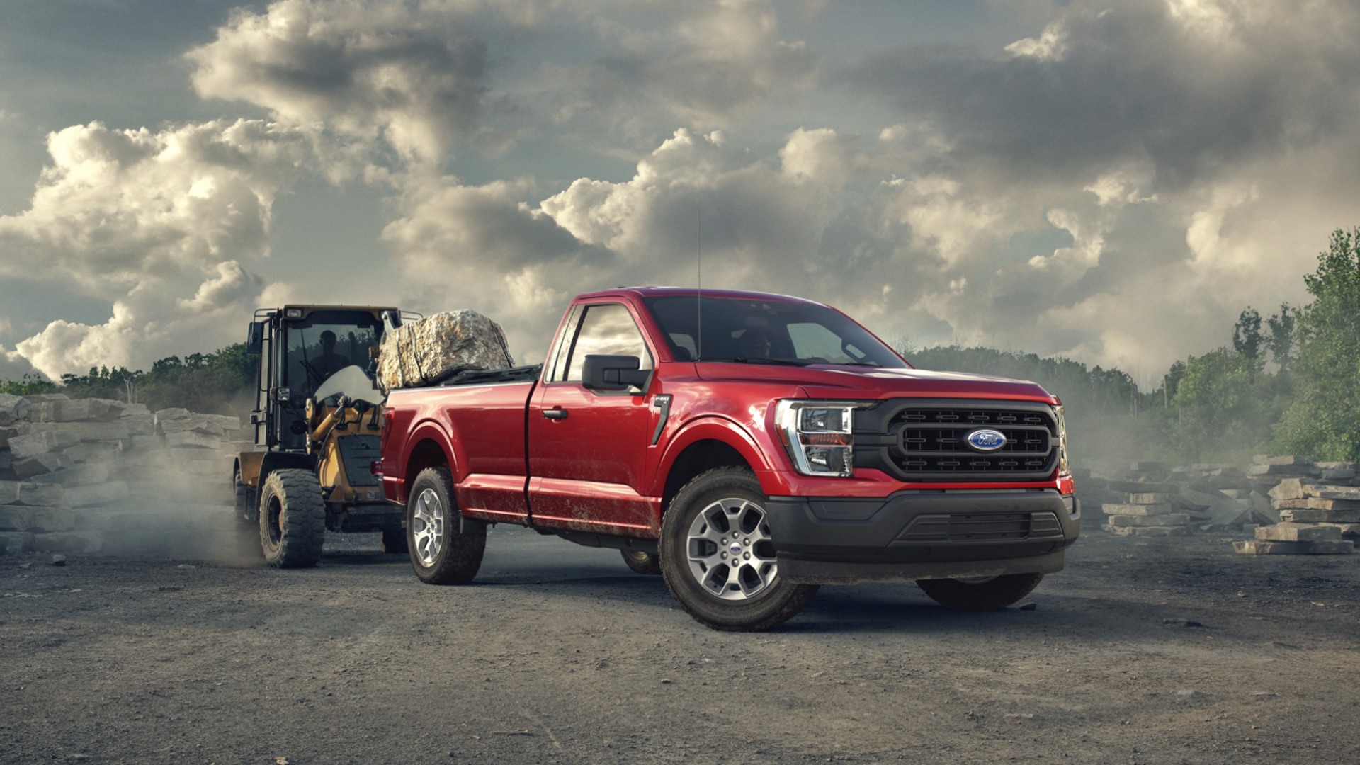 Red Ford pickup truck parked on a construction site with a loader in the background.
