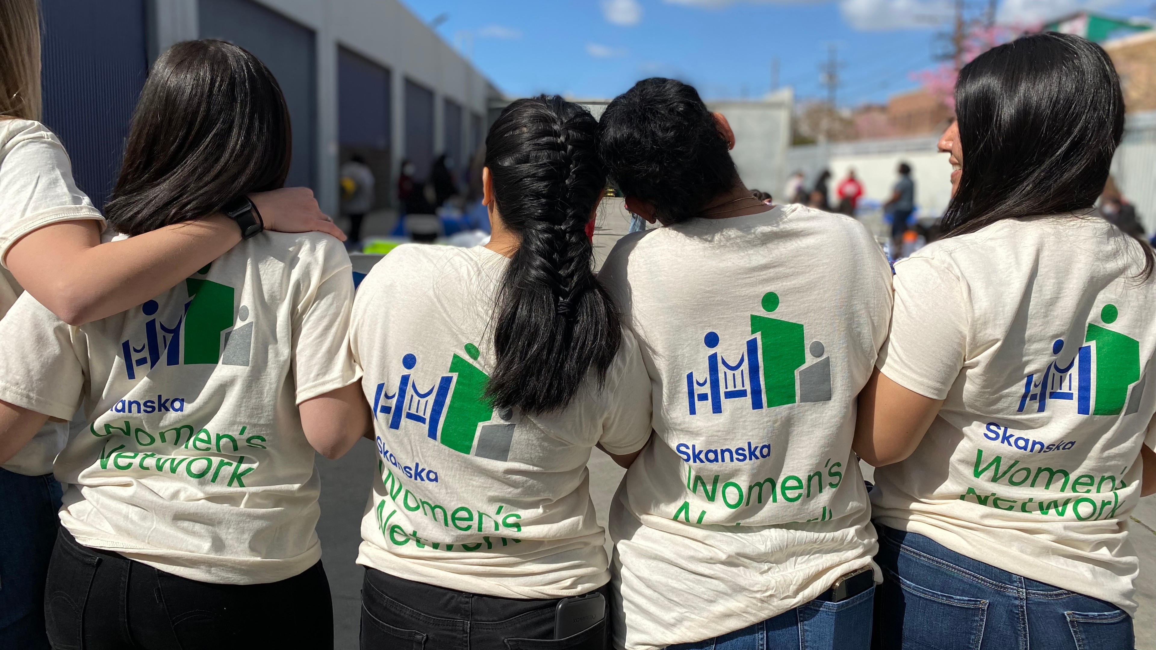 Group of women wearing Skanska Women's Network t-shirts standing outdoors with blue sky.