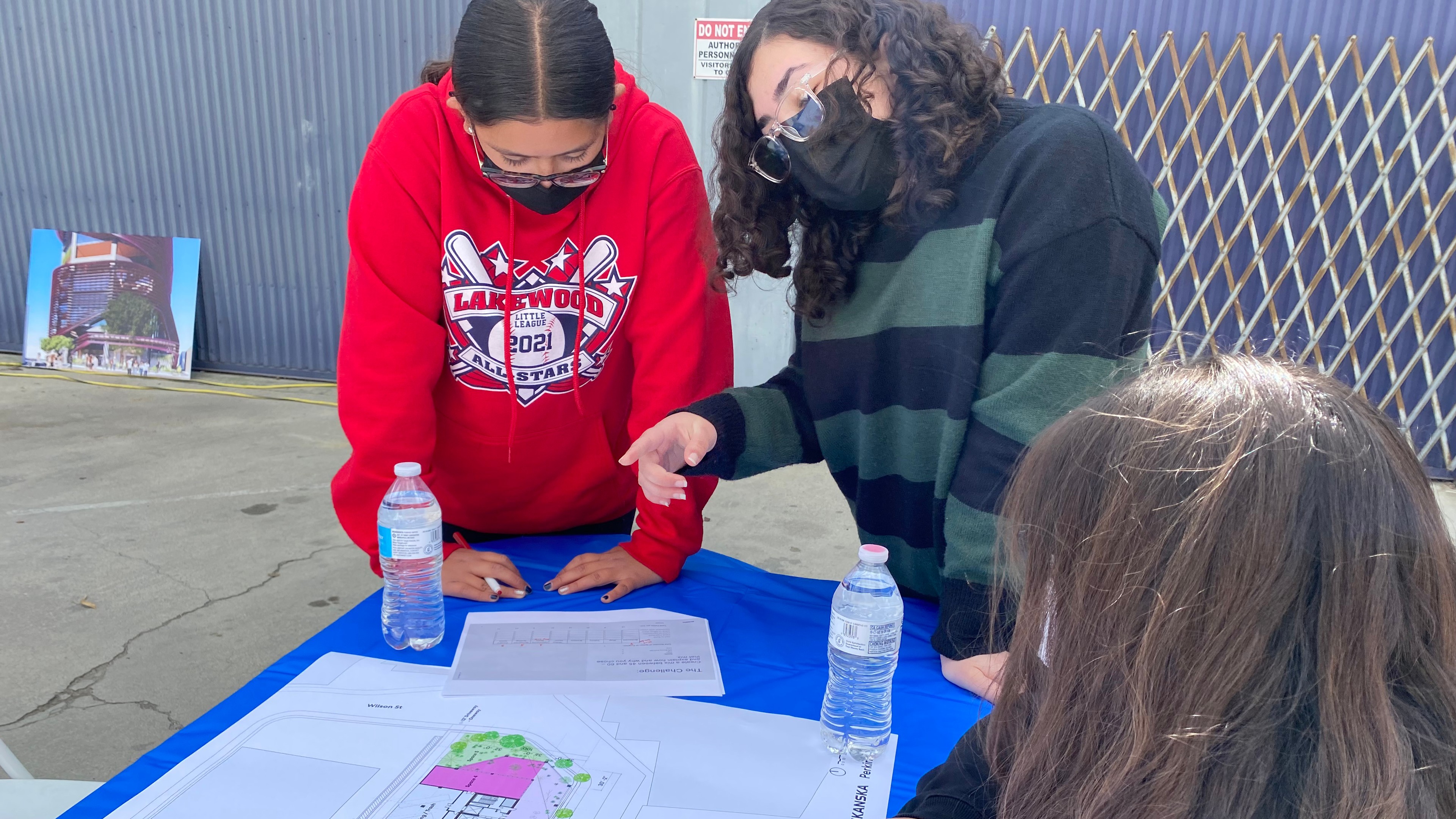 Three people discussing architectural plans on a table outdoors with water bottles.