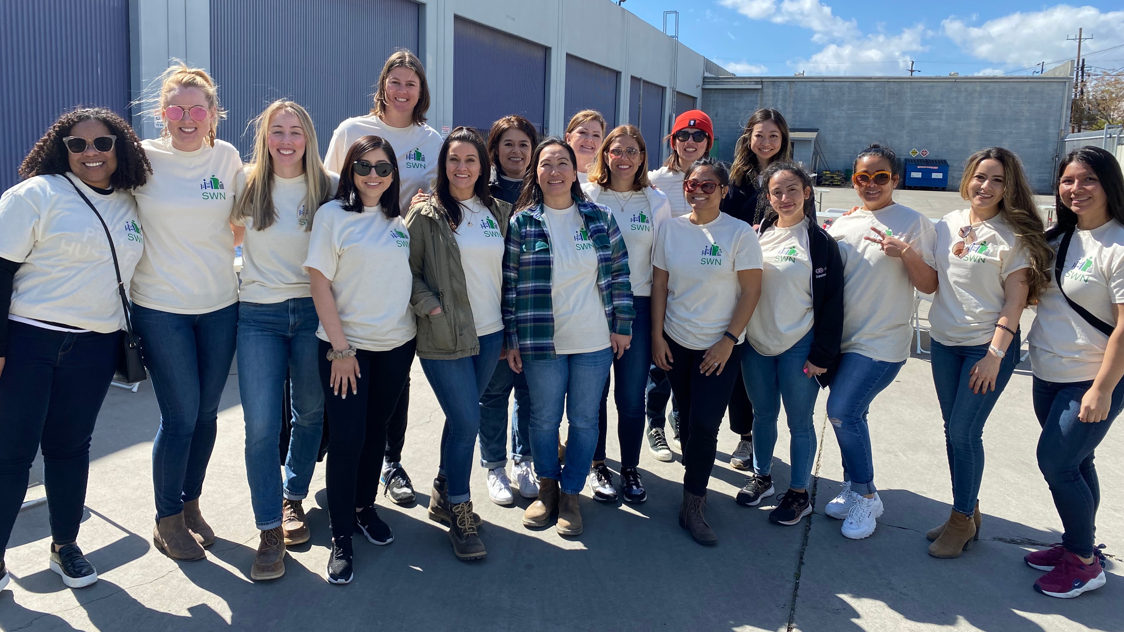 Group of diverse people wearing matching white t-shirts standing outdoors on a sunny day.