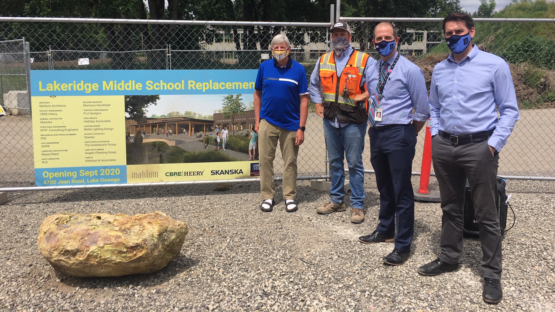 Four men standing in front of a construction sign for Lakeridge Middle School replacement.