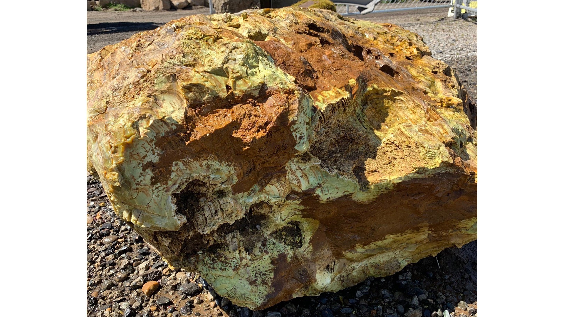 Large rough yellow and brown sulfur rock on gravel surface in outdoor setting.