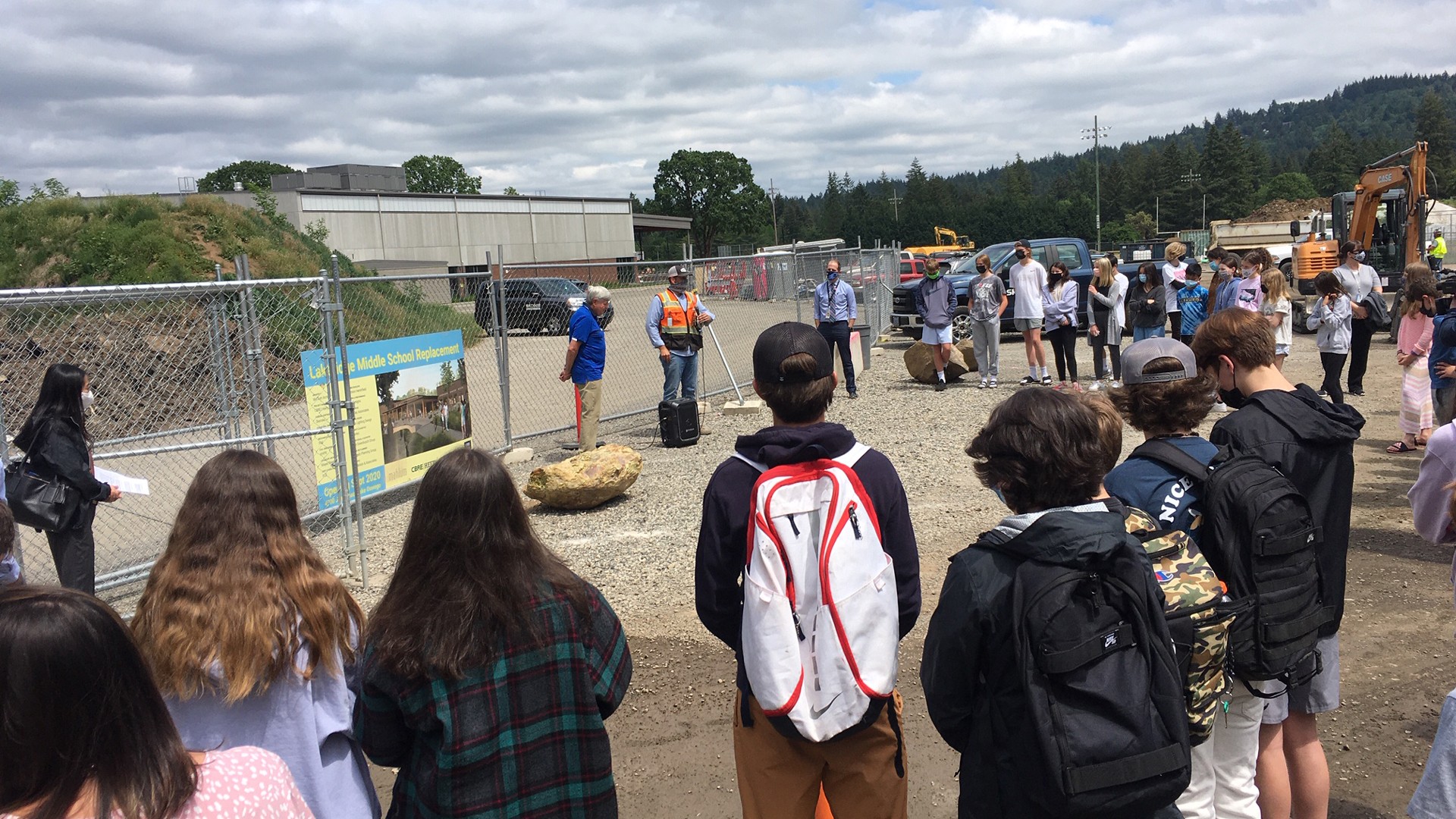 Group of students and adults gathered at a school construction site for an outdoor event.