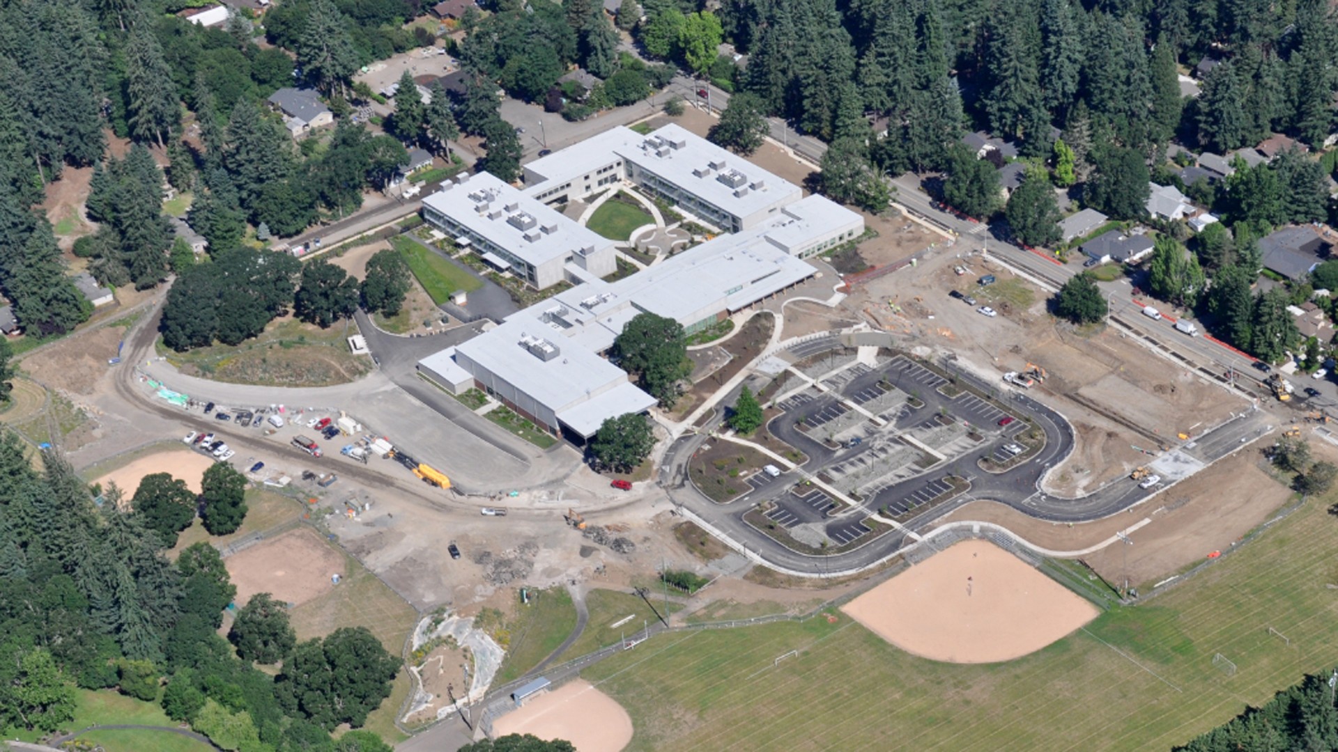 Aerial view of a school building surrounded by parking lots, sports fields, and trees.