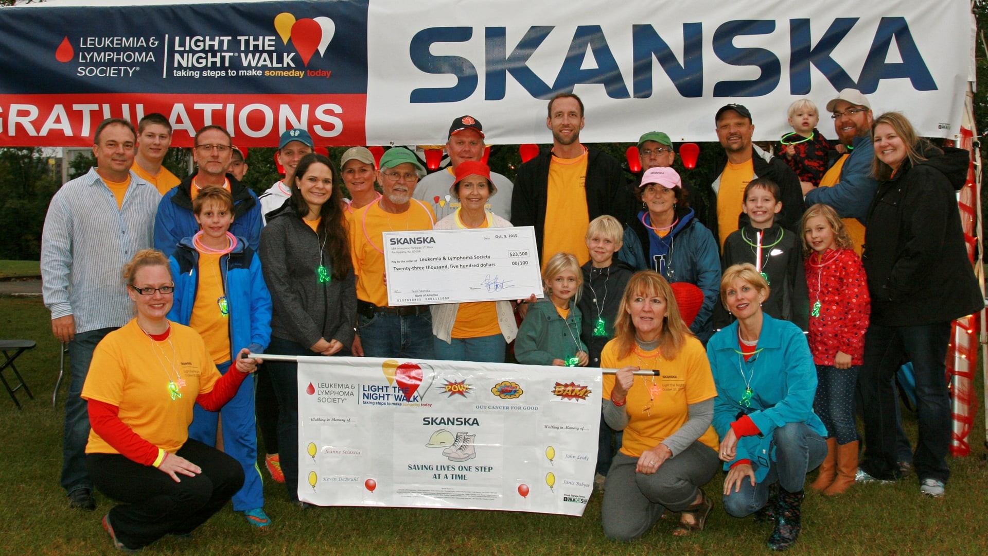 Group of people at a charity event holding a large check and banner for leukemia awareness.