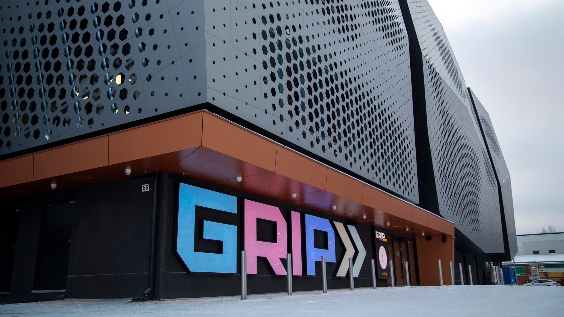 Moderni rakennuksen julkisivu, jossa suuret värikkäät "GRIP"-kirjaimet mustalla perforoidulla julkisivulla.