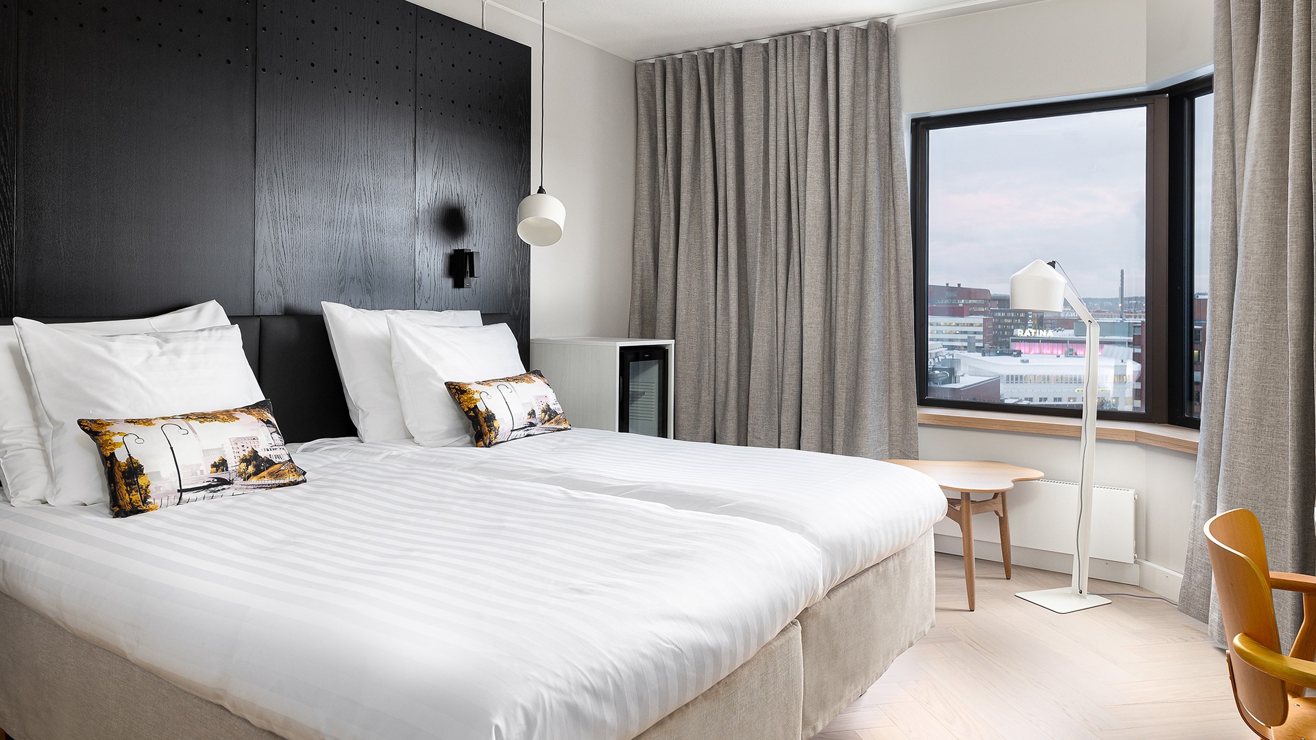 Moderni hotellihuone, jossa on kaksi erillistä vuodetta, valkoiset vuodevaatteet, suuri ikkuna ja neutraali sisustus.