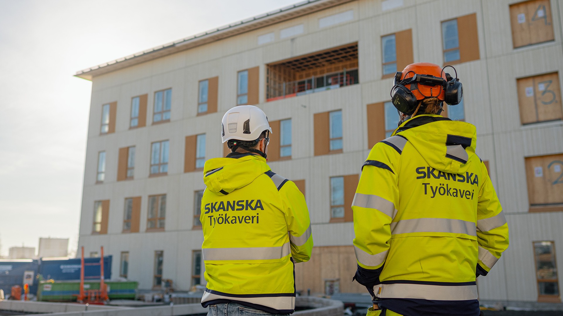 Kaksi rakennustyöntekijää työtakeissa, joissa lukee Työkaveri, seisovat rakennustyömaalla.