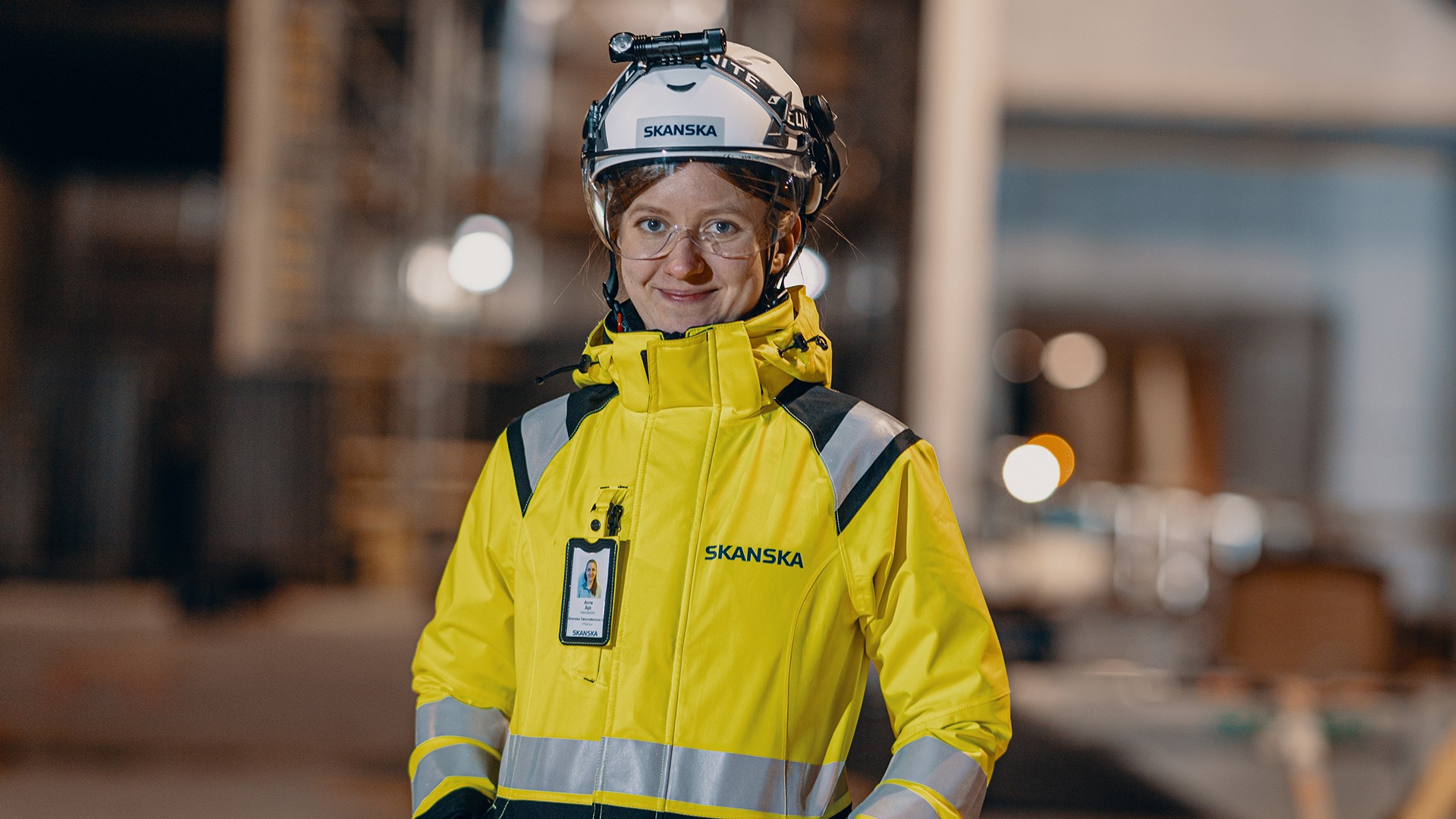 Construction worker in a Skanska-branded high-visibility jacket and helmet at a building site.
