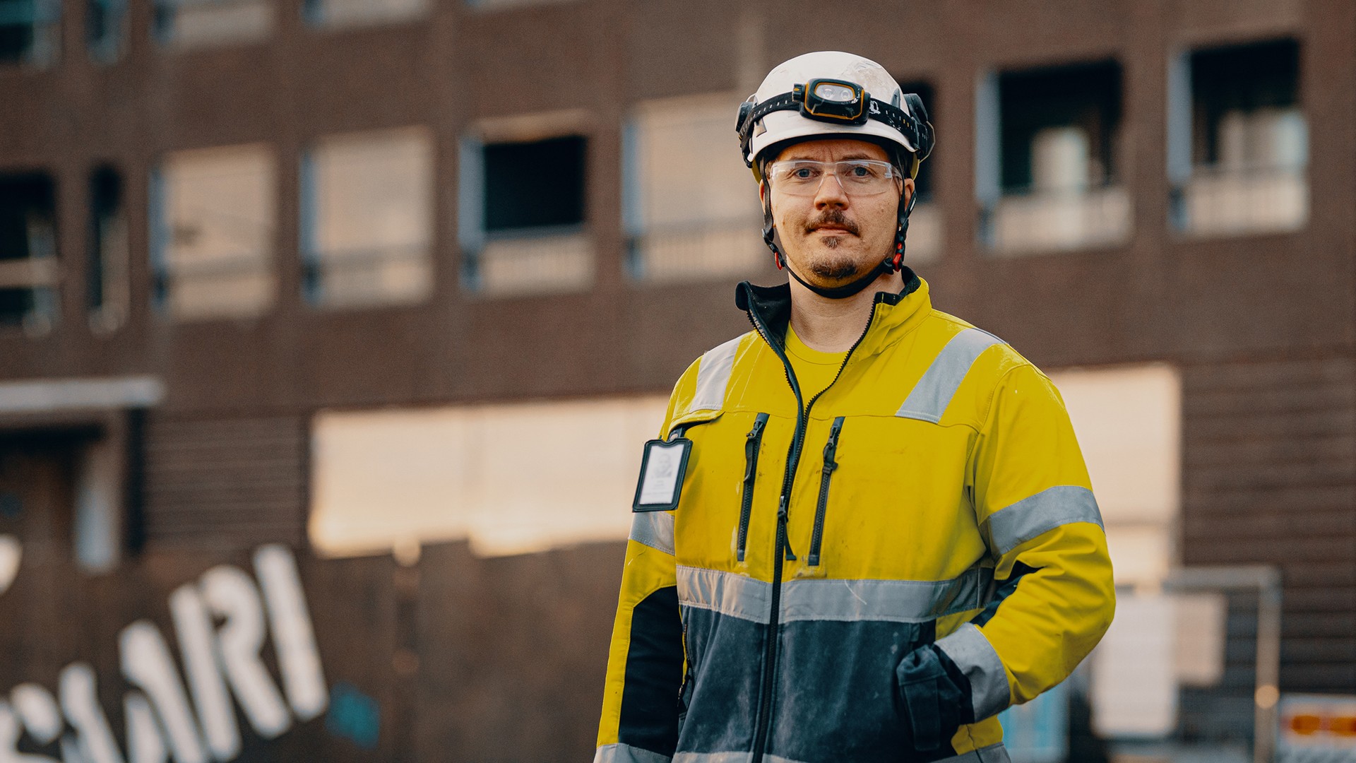 Rakennustyöntekijä, joka käyttää turvakypärää ja heijastavaa takkia työmaalla.