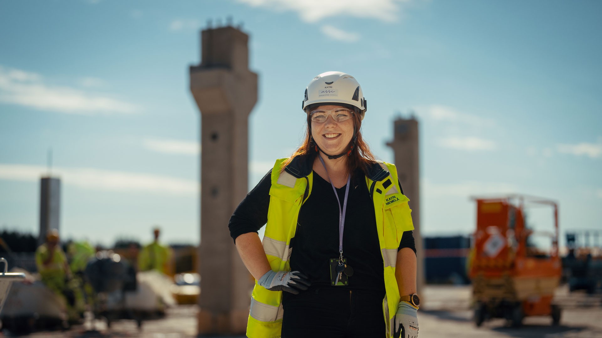 Construction worker in safety gear stands confidently on a site with pillars in the background.