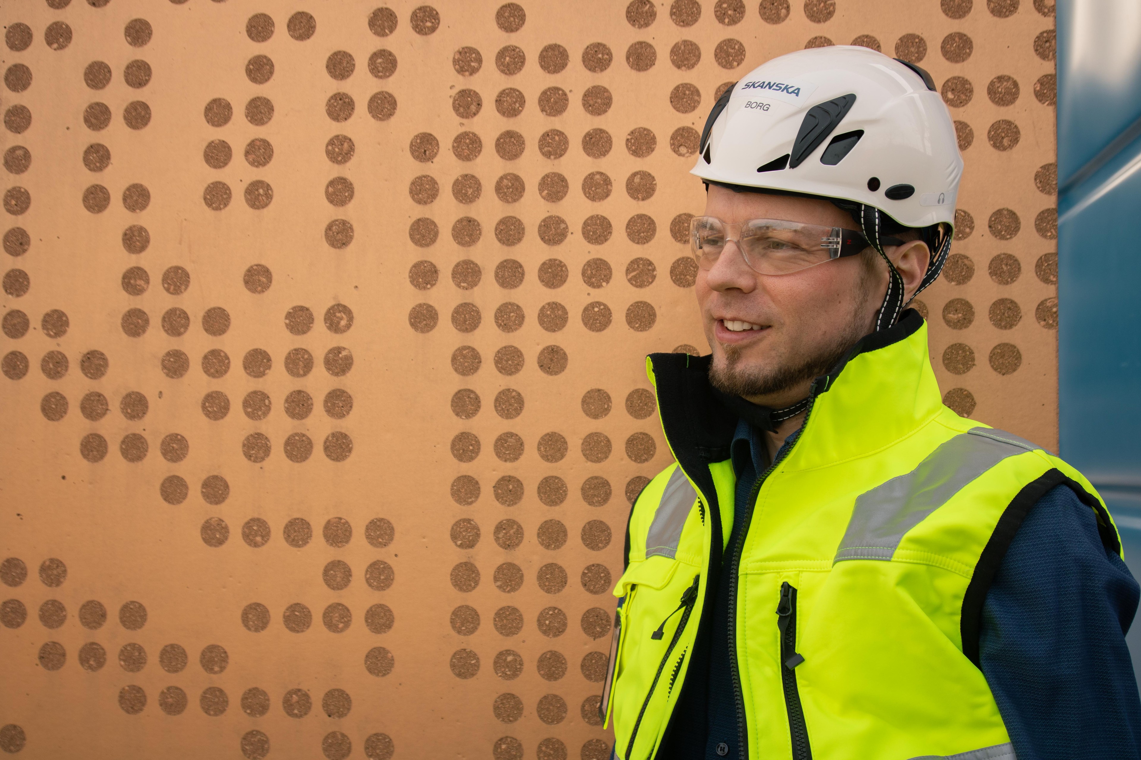 Rakennustyöntekijä, jolla on valkoinen kypärä ja keltainen korkean näkyvyyden turvaliivi.