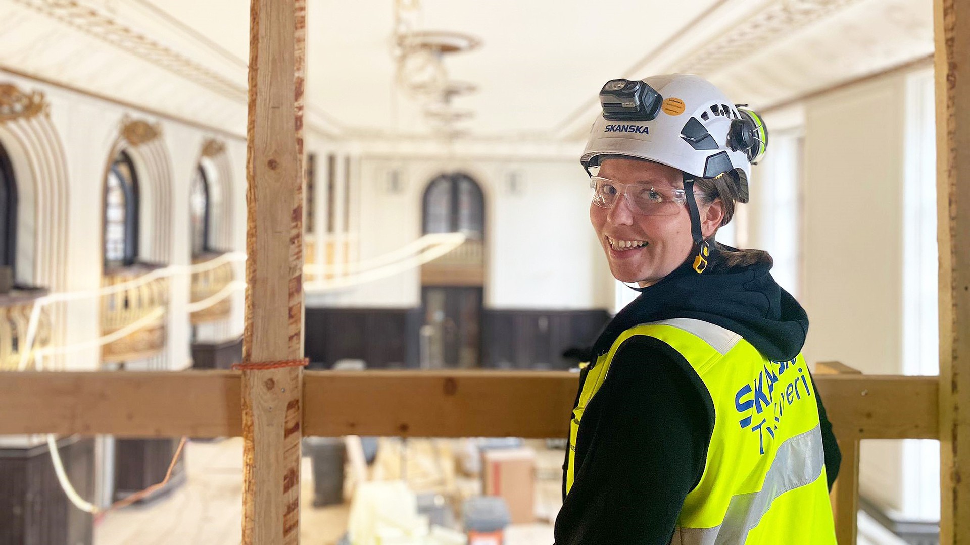 Construction worker in Skanska gear observing historic building renovation progress.