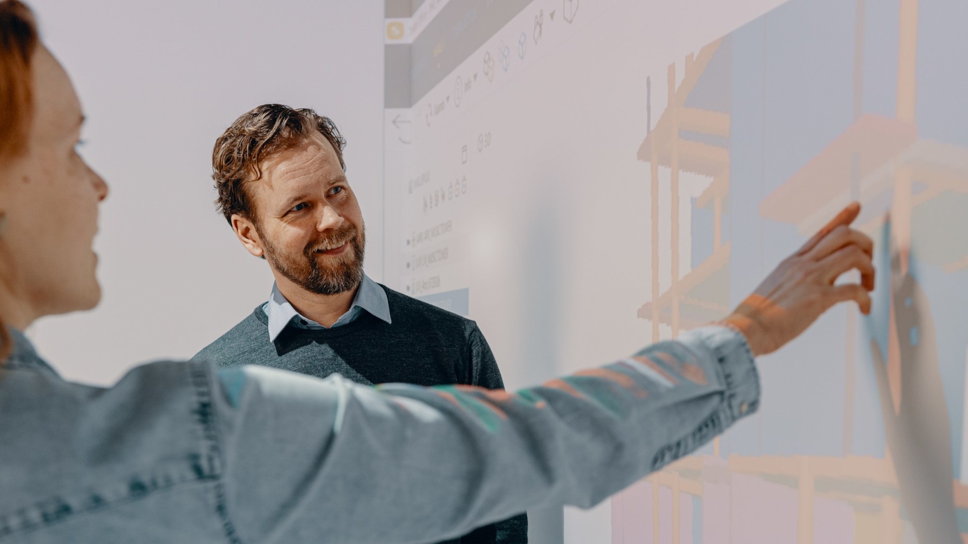 Person pointing at a projected screen during a presentation or discussion in a modern office setting.
