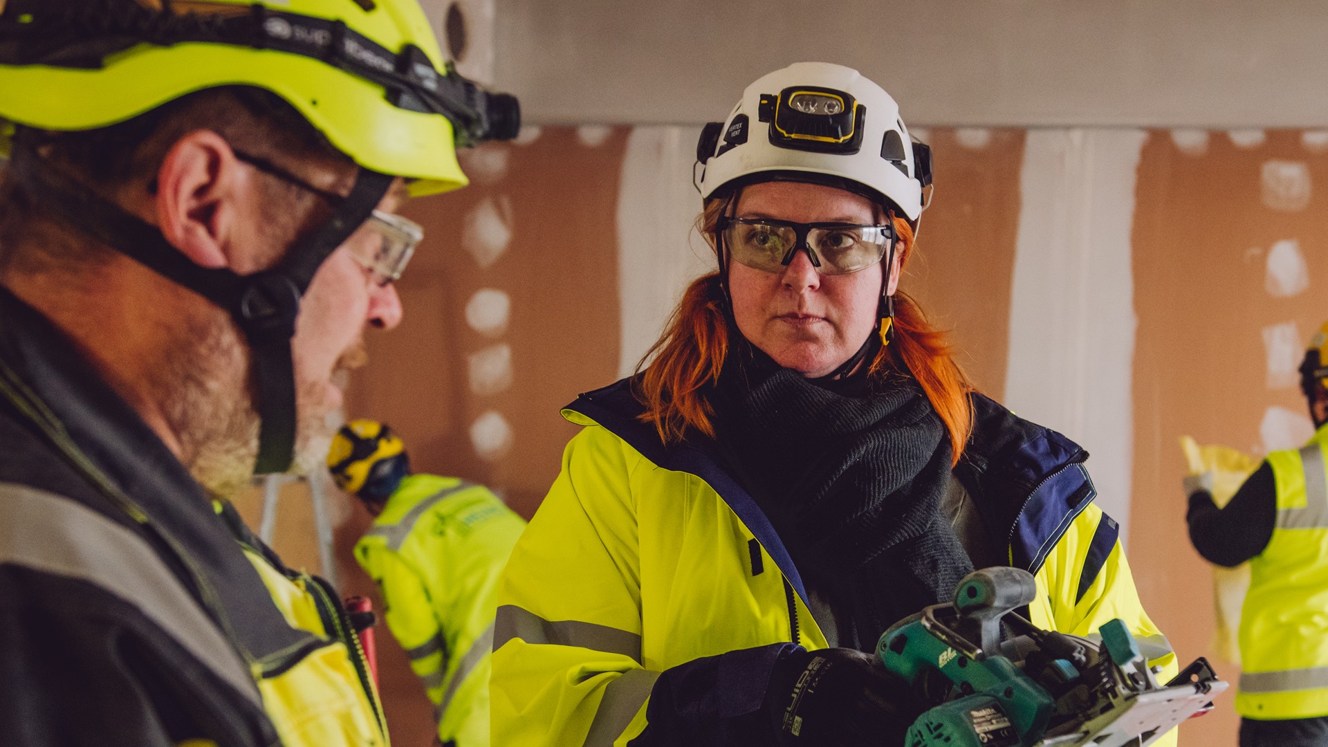 Rakennustyöntekijät turvavarusteissa käyttävät sähkötyökaluja sisätiloissa rakennustyömaalla.