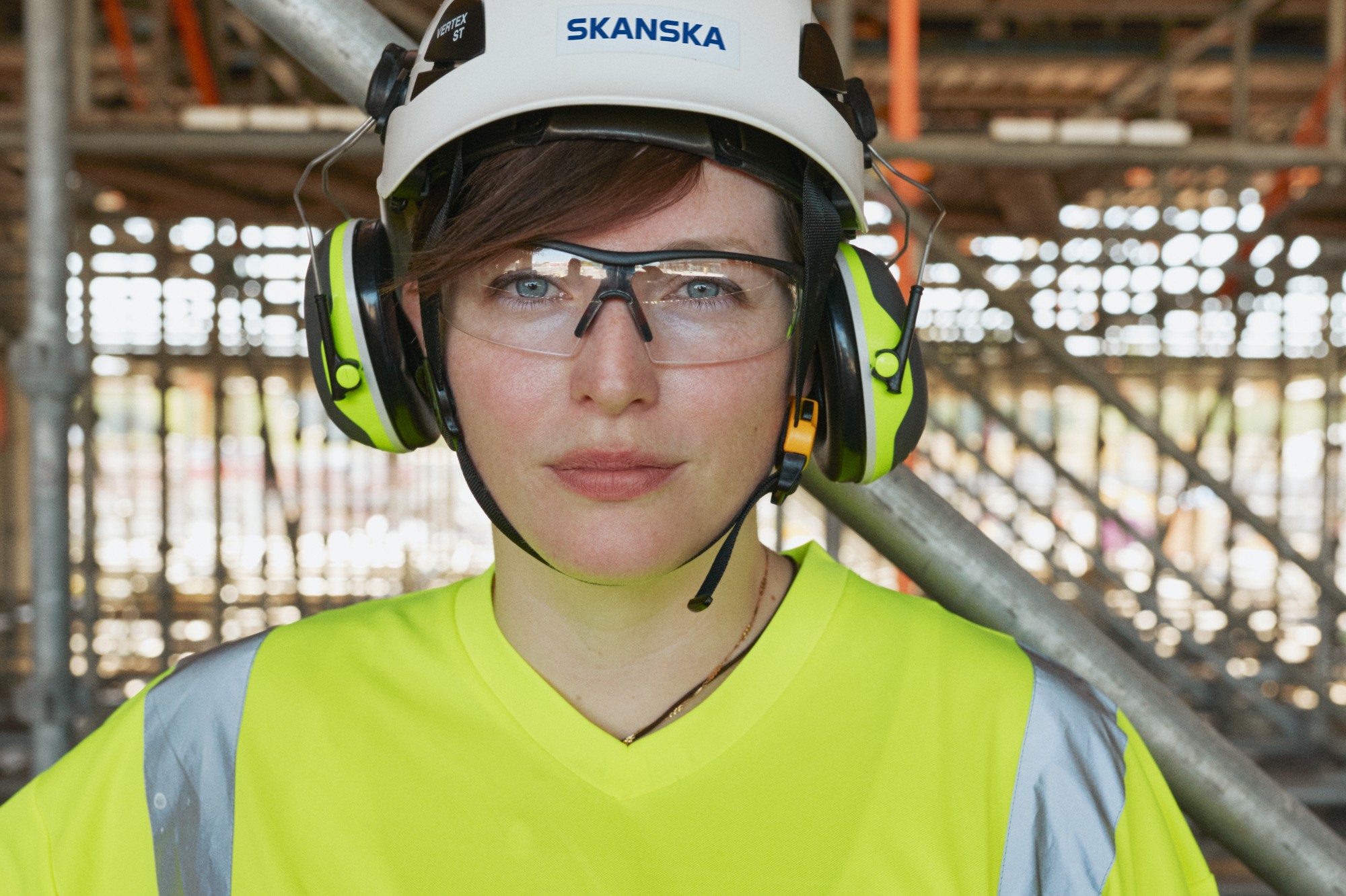 Construction worker wearing safety gear, including a helmet labeled "Skanska" and ear protection.