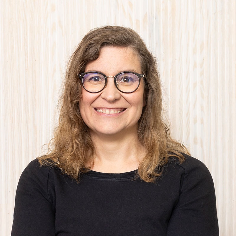 Smiling person with long, curly hair and a black blouse.