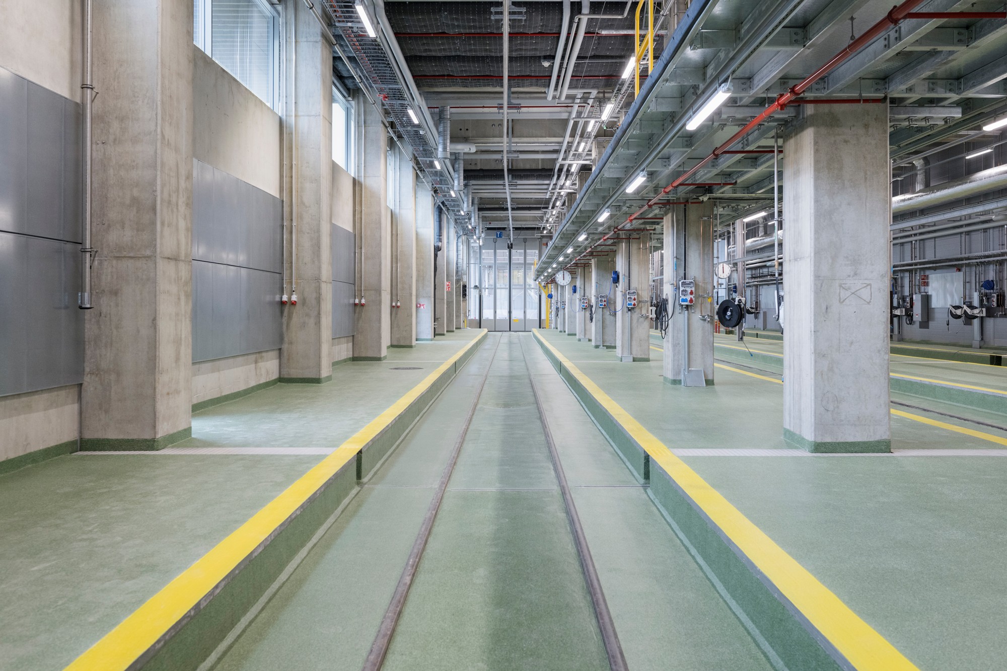 Modern industrial facility with tracks, concrete columns, and overhead piping systems.