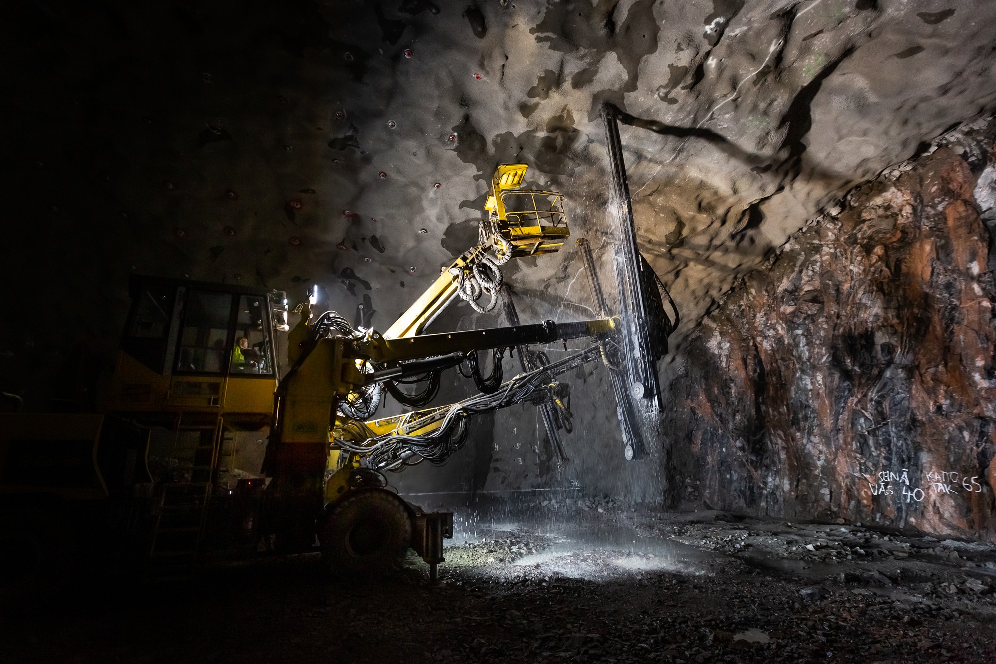 A large industrial drilling machine operates in a dimly lit underground tunnel, carving into the rocky surface.