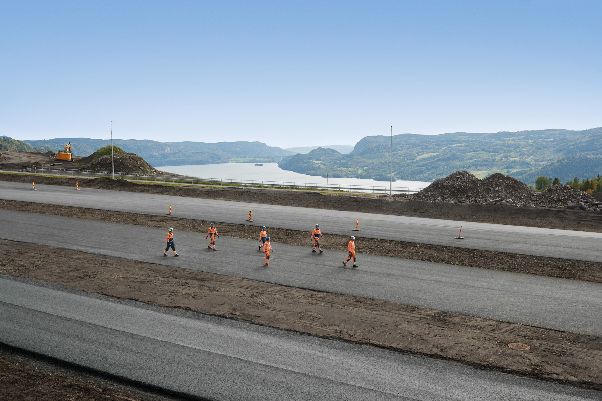 Construction workers in orange safety gear walking on a newly paved road with mountains.