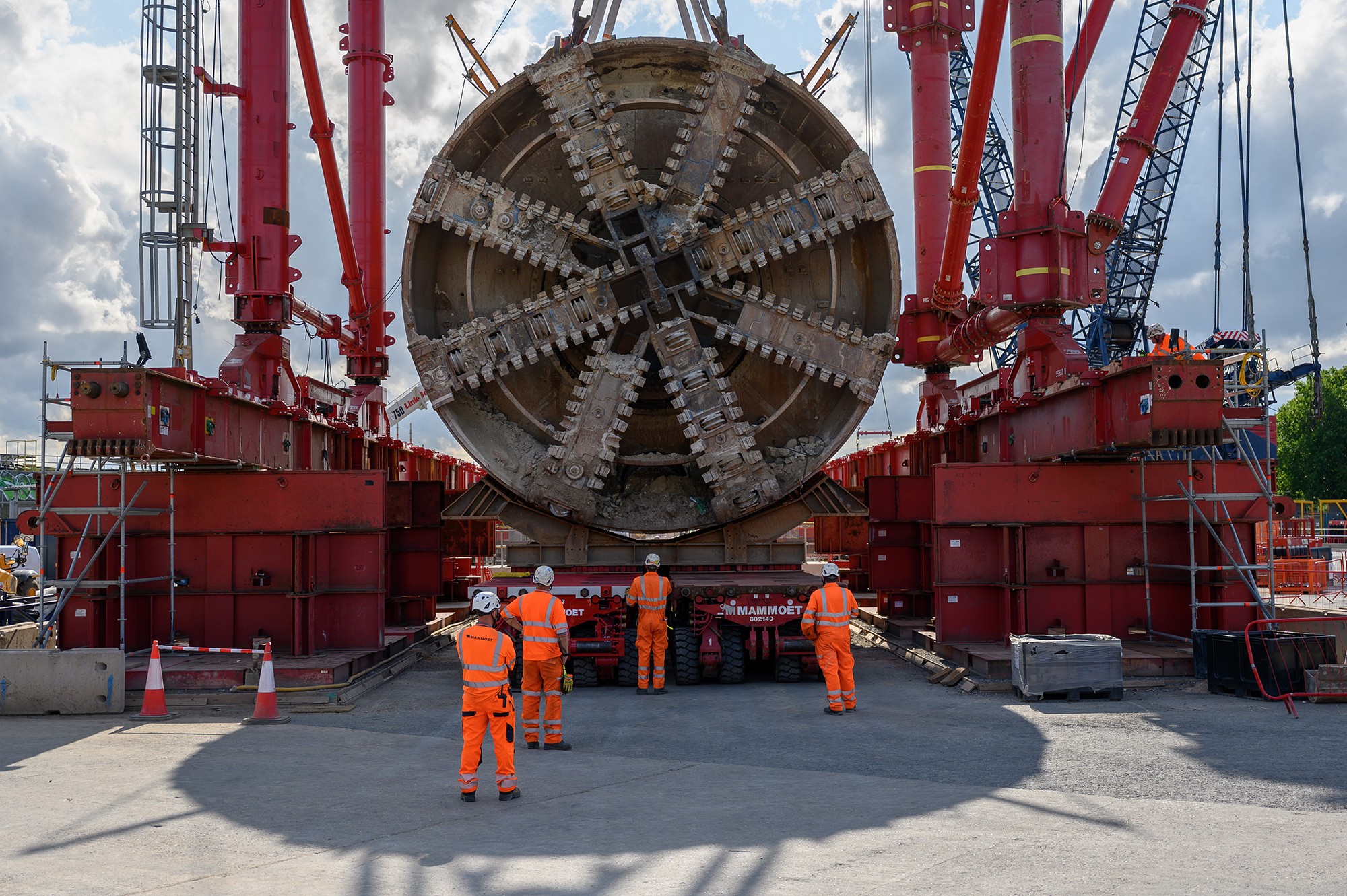 Large tunnel boring machine head being transported at construction site with workers.