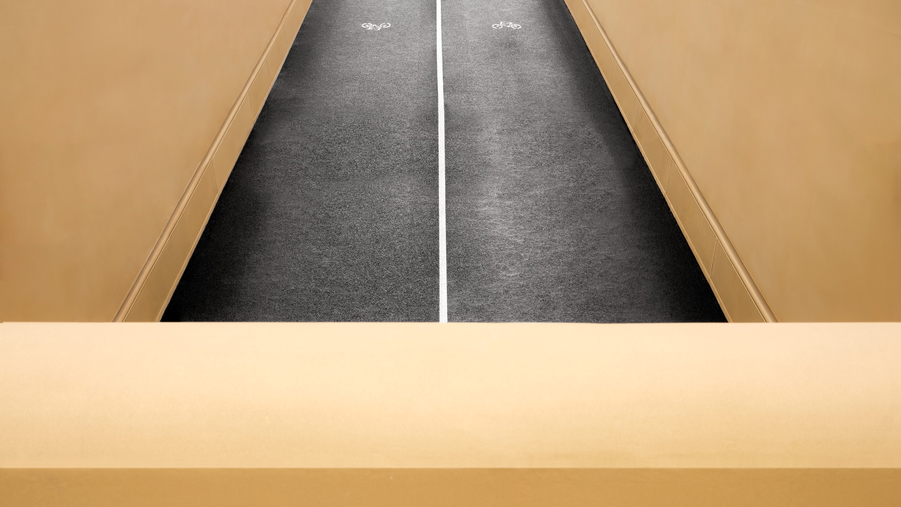 Aerial view of a narrow, empty bicycle path with beige walls and a dividing white line.