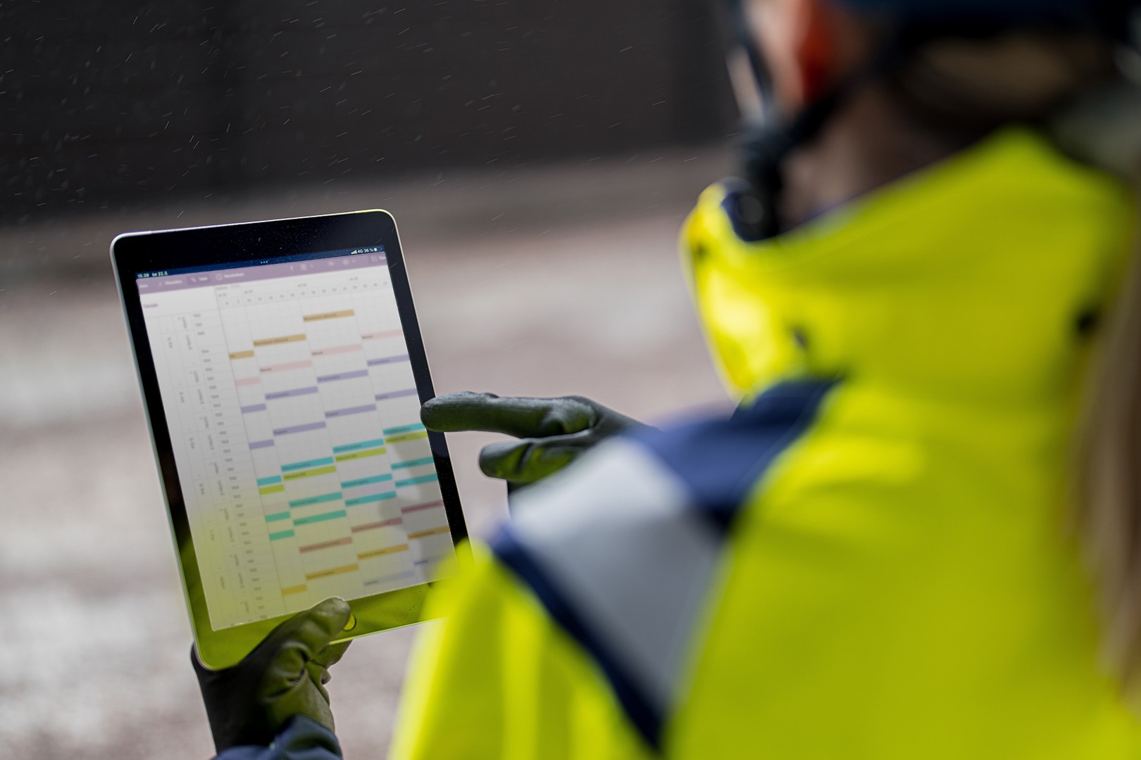 Person in high-visibility jacket using a tablet displaying a colorful schedule chart.