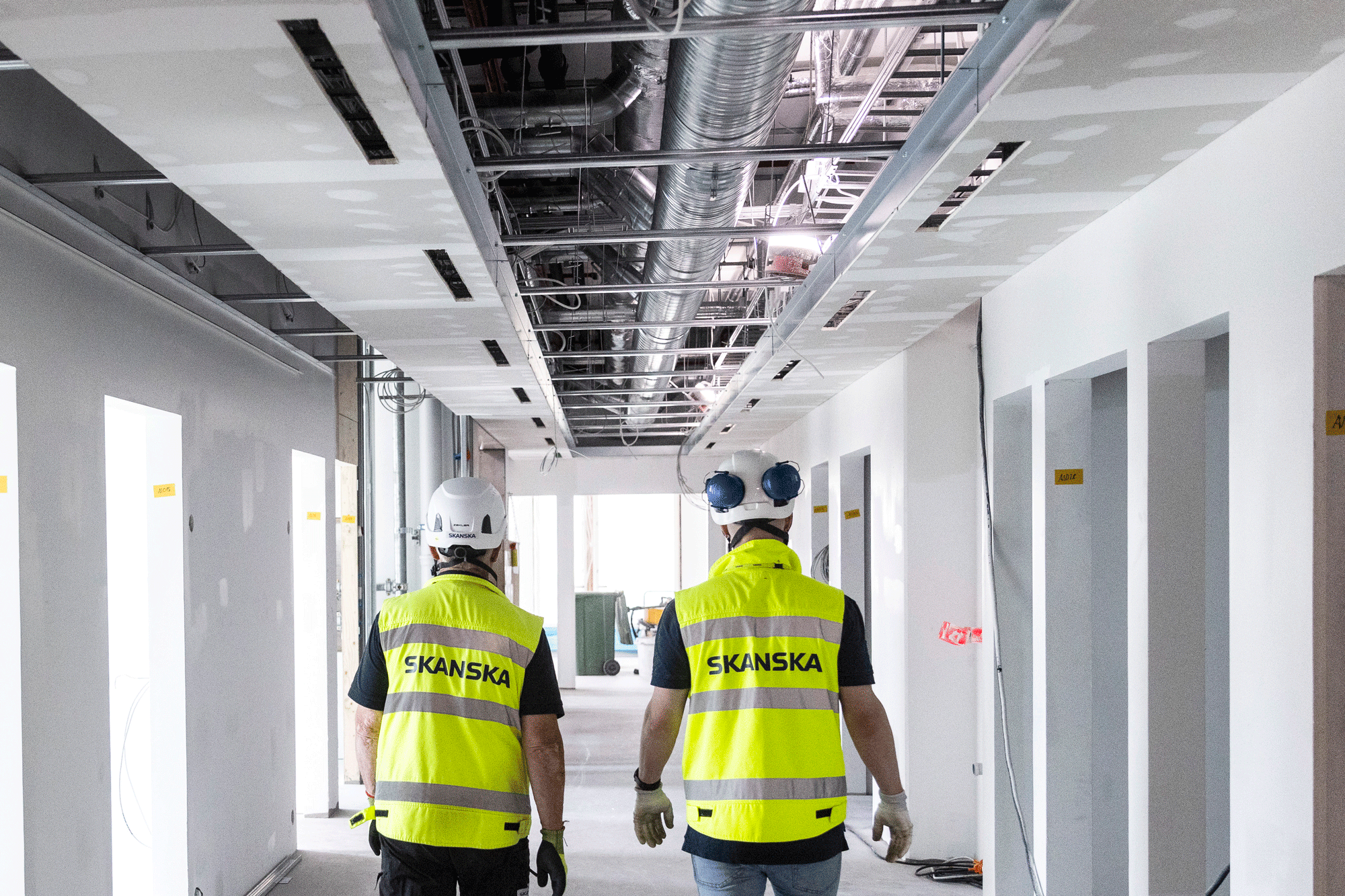 Two construction workers in Skanska vests walk through a building under construction.