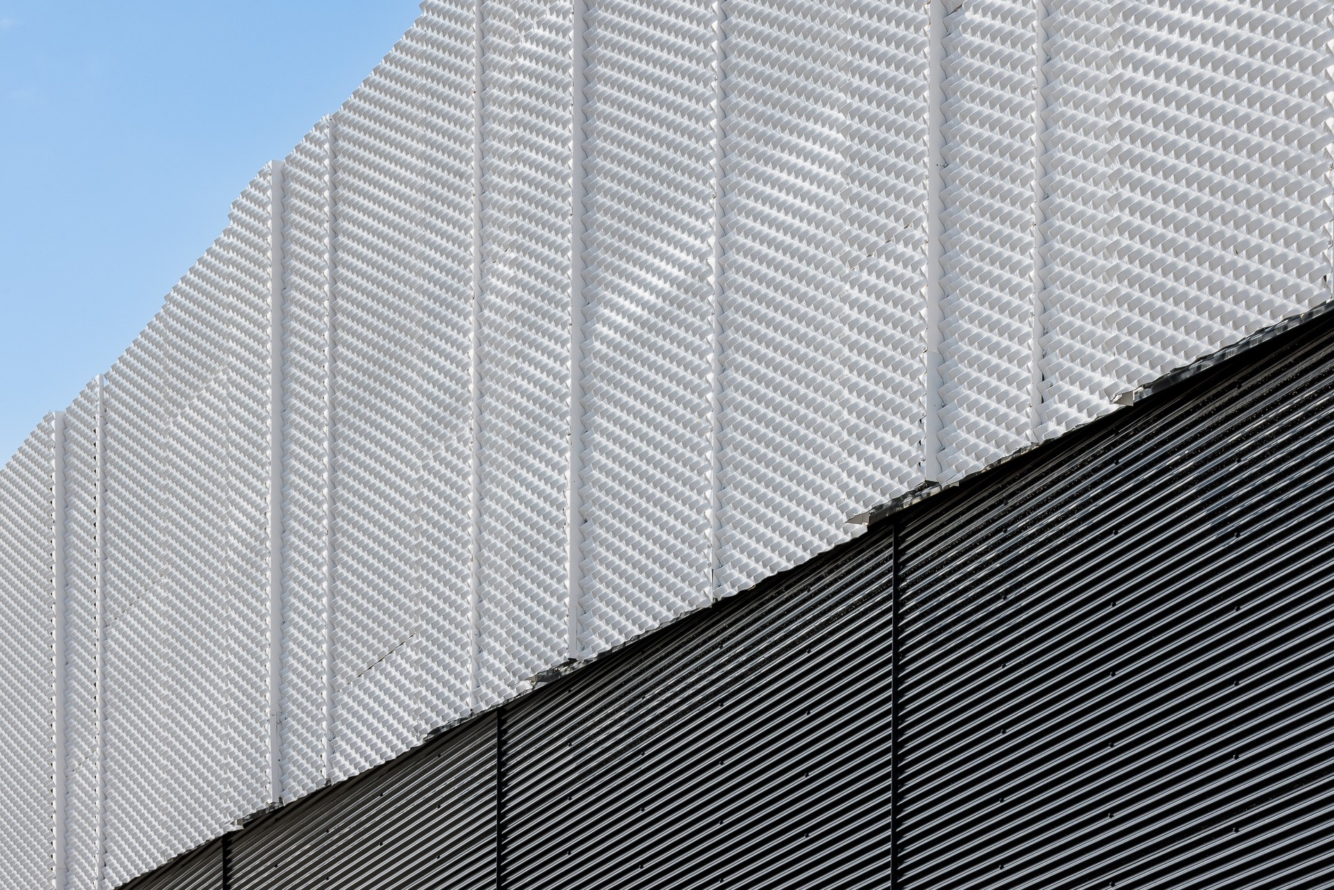 Modern building facade with textured white panels above horizontal dark lines against blue sky.