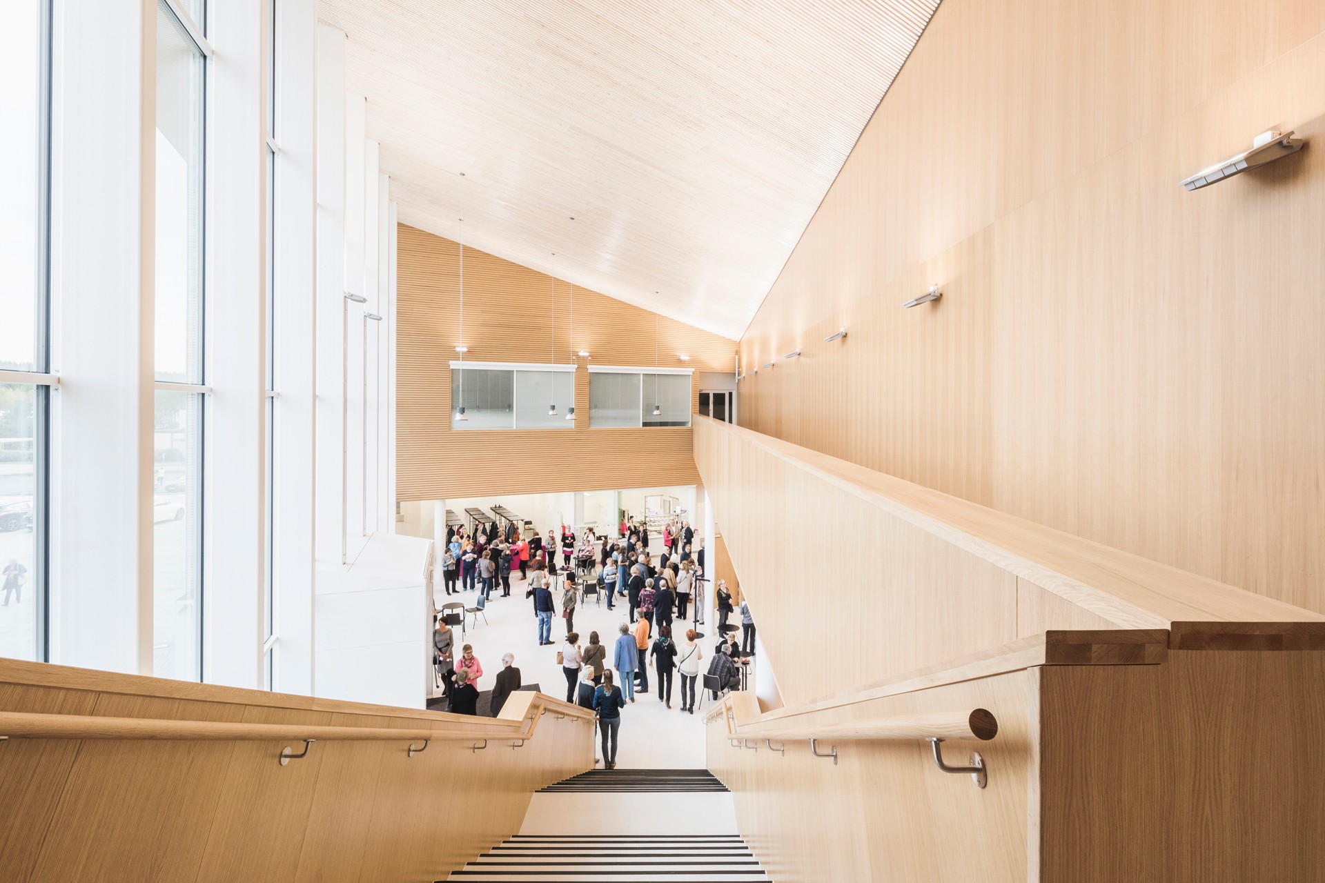 Modern interior staircase leading to a spacious, bright lobby with people gathered in groups.