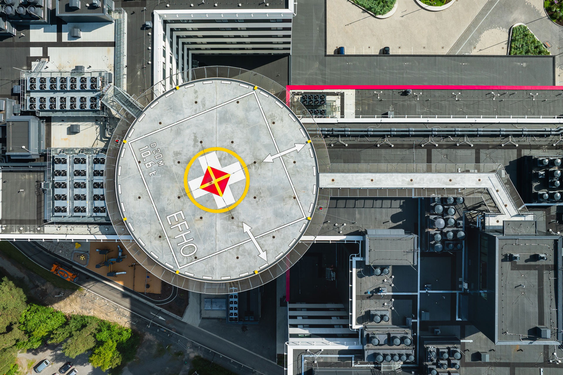 Aerial view of a helipad marked "EHO," surrounded by modern buildings with rooftop equipment.