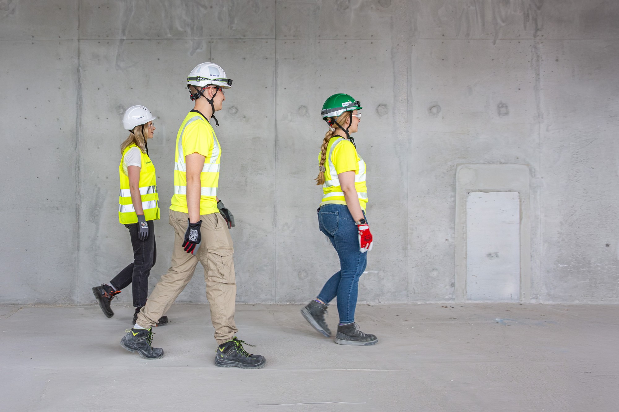 Three construction workers wearing helmets and reflective vests walking inside a building.