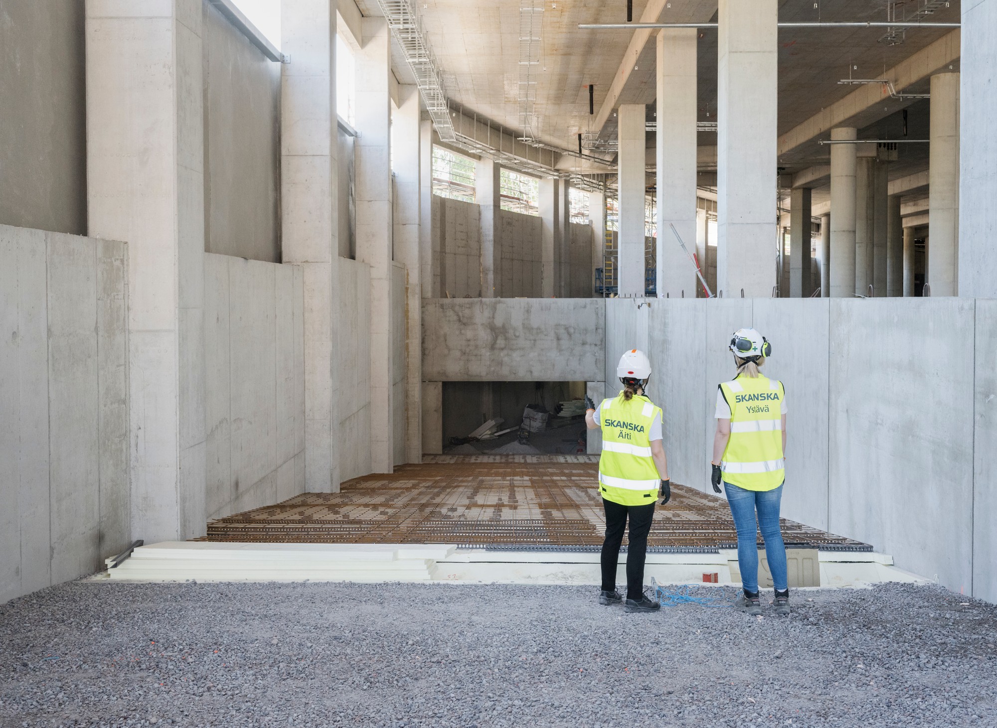 Kaksi rakennustyöntekijää turvavarusteissa tarkastaa rakenteilla olevaa suurta betonirakennelmaa.