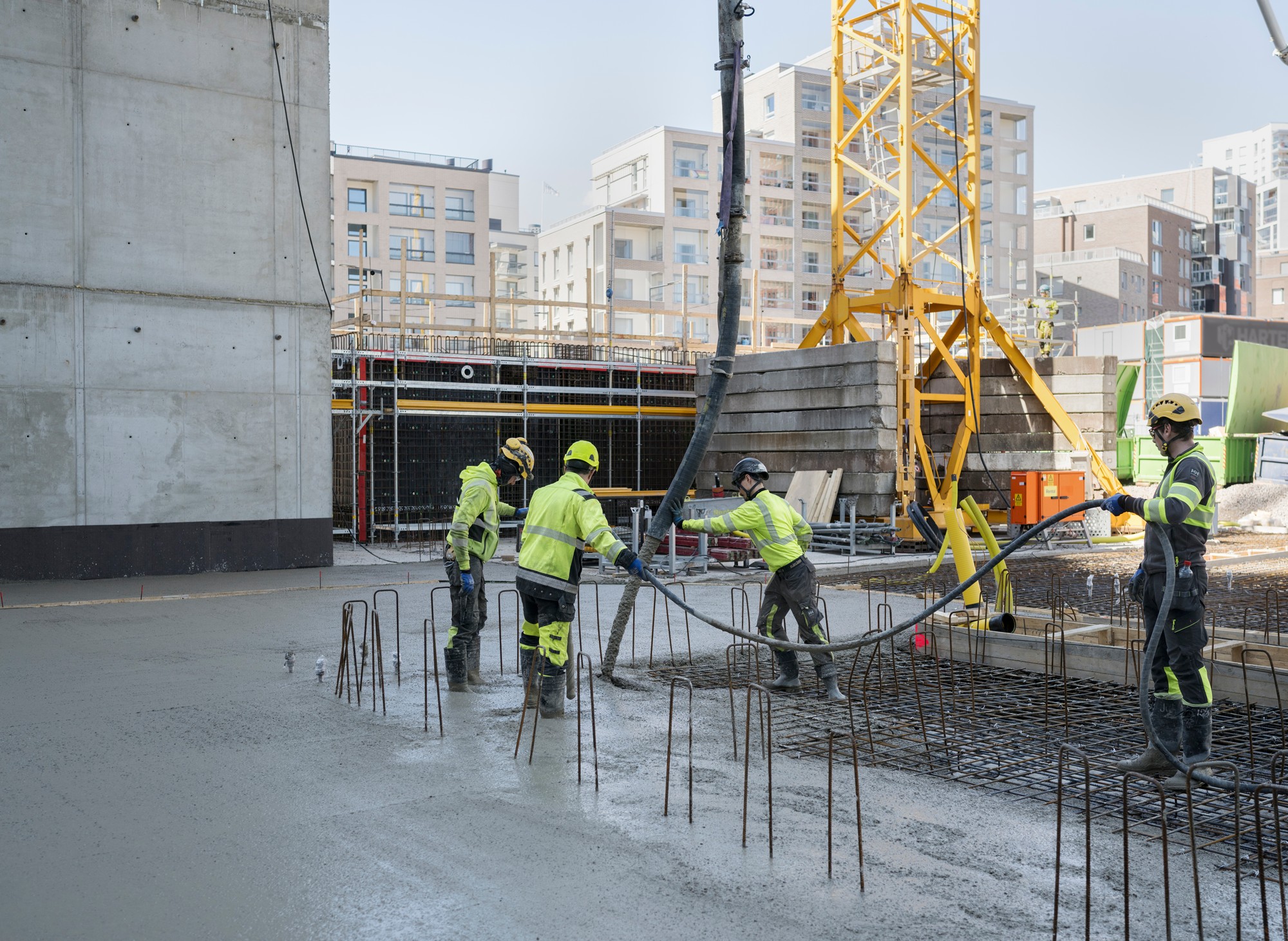 Rakennustyöntekijät kaatavat betonia rakennustyömaalla, ympärillään rakennustelineitä ja laitteita.