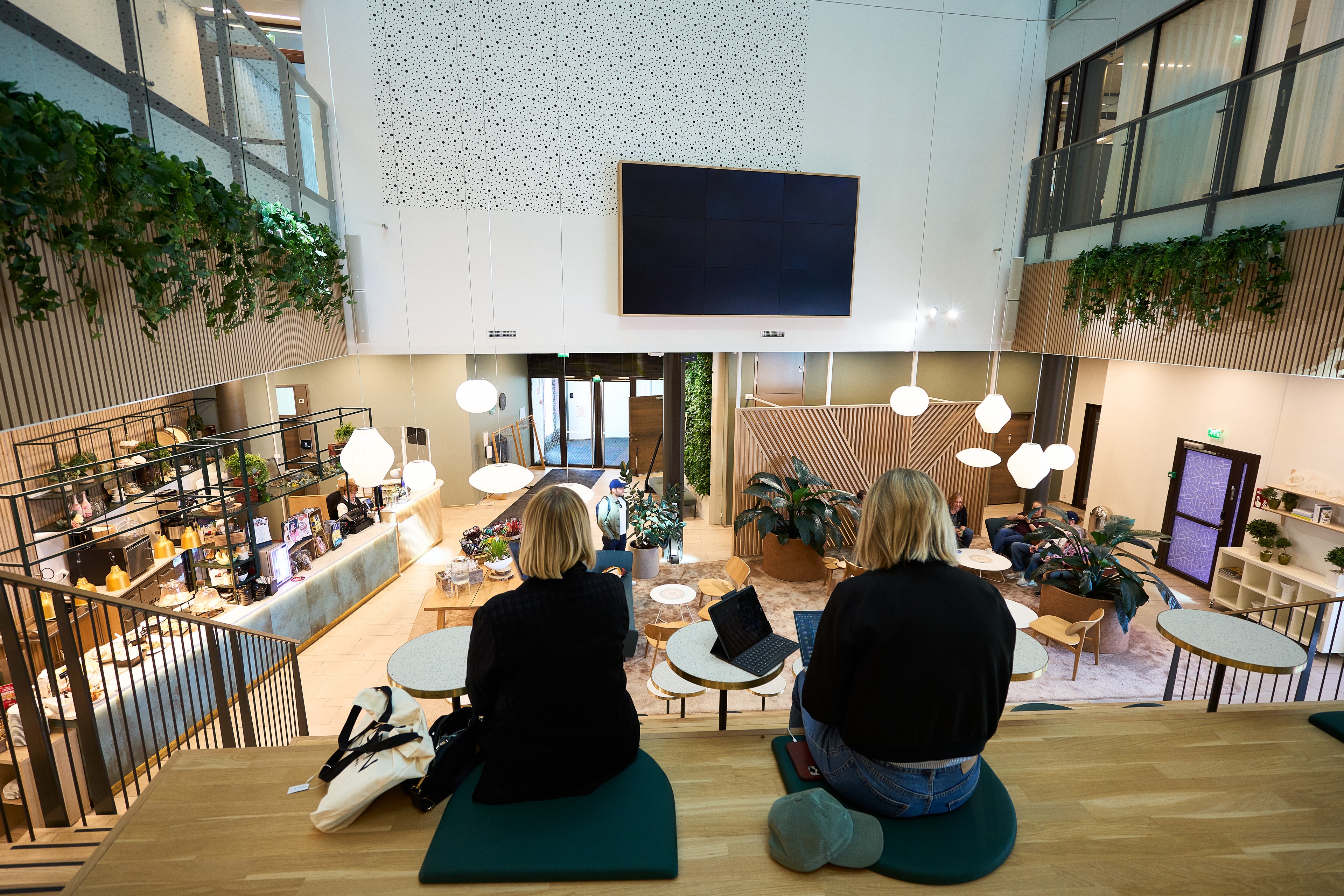 Two women sitting on cushions in a modern, plant-decorated co-working space with laptops.